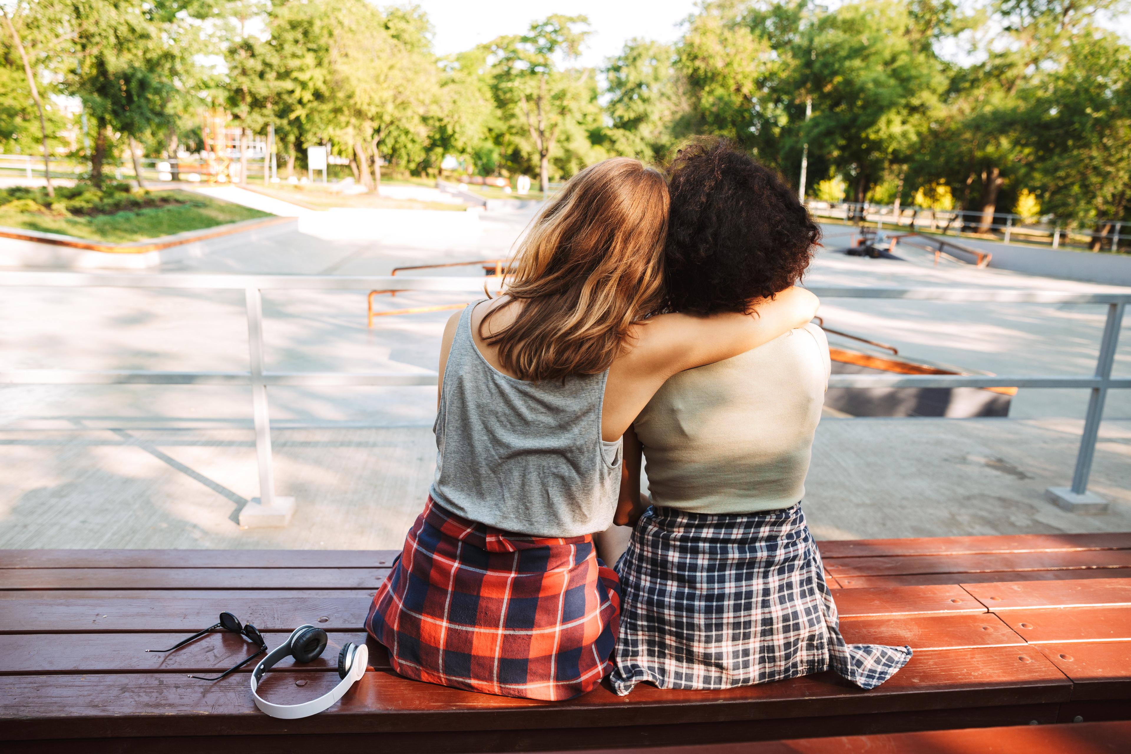 Two female friends sit with arms around each other, backs to the camera