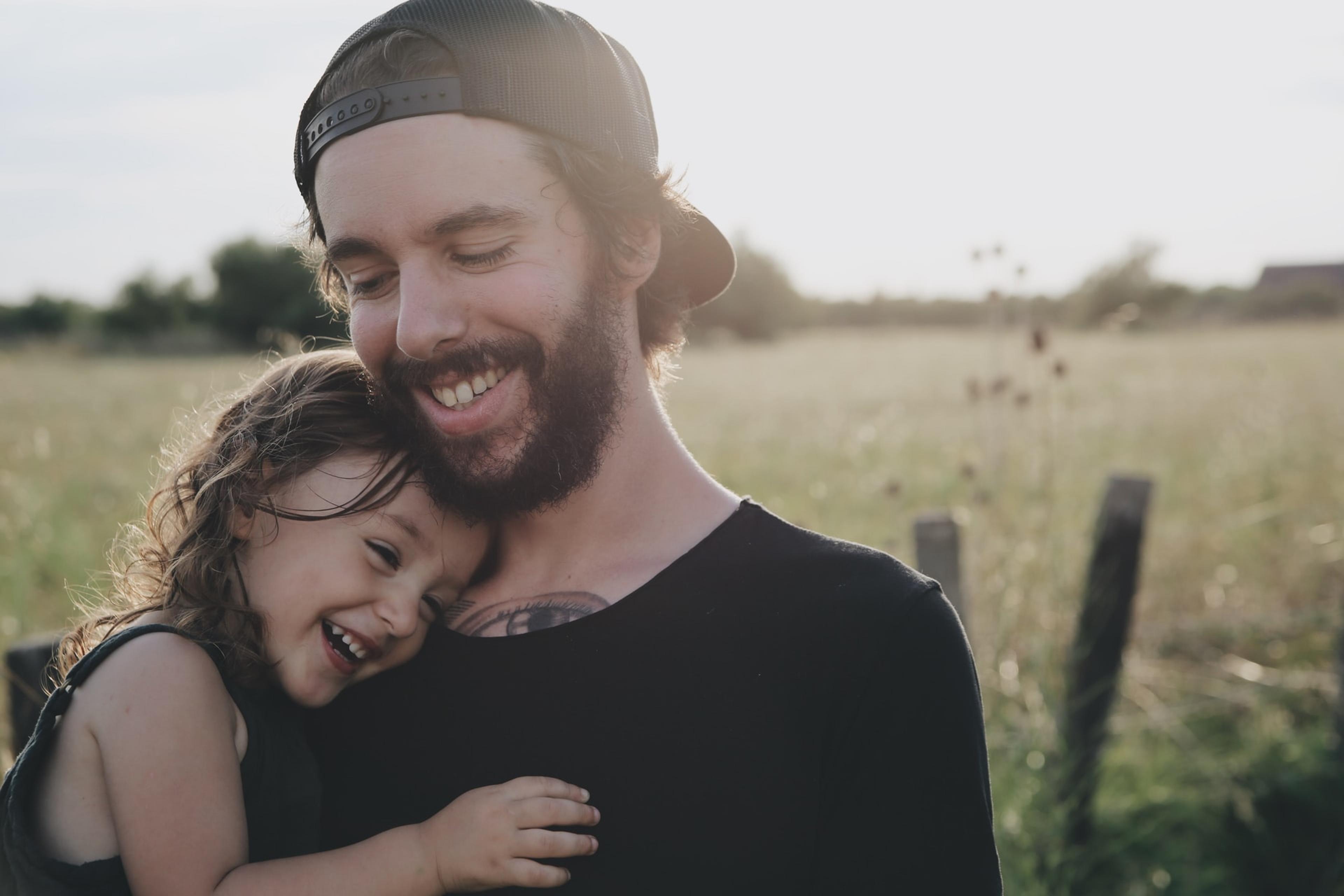 A young father hugs his young daughter in a sunny field