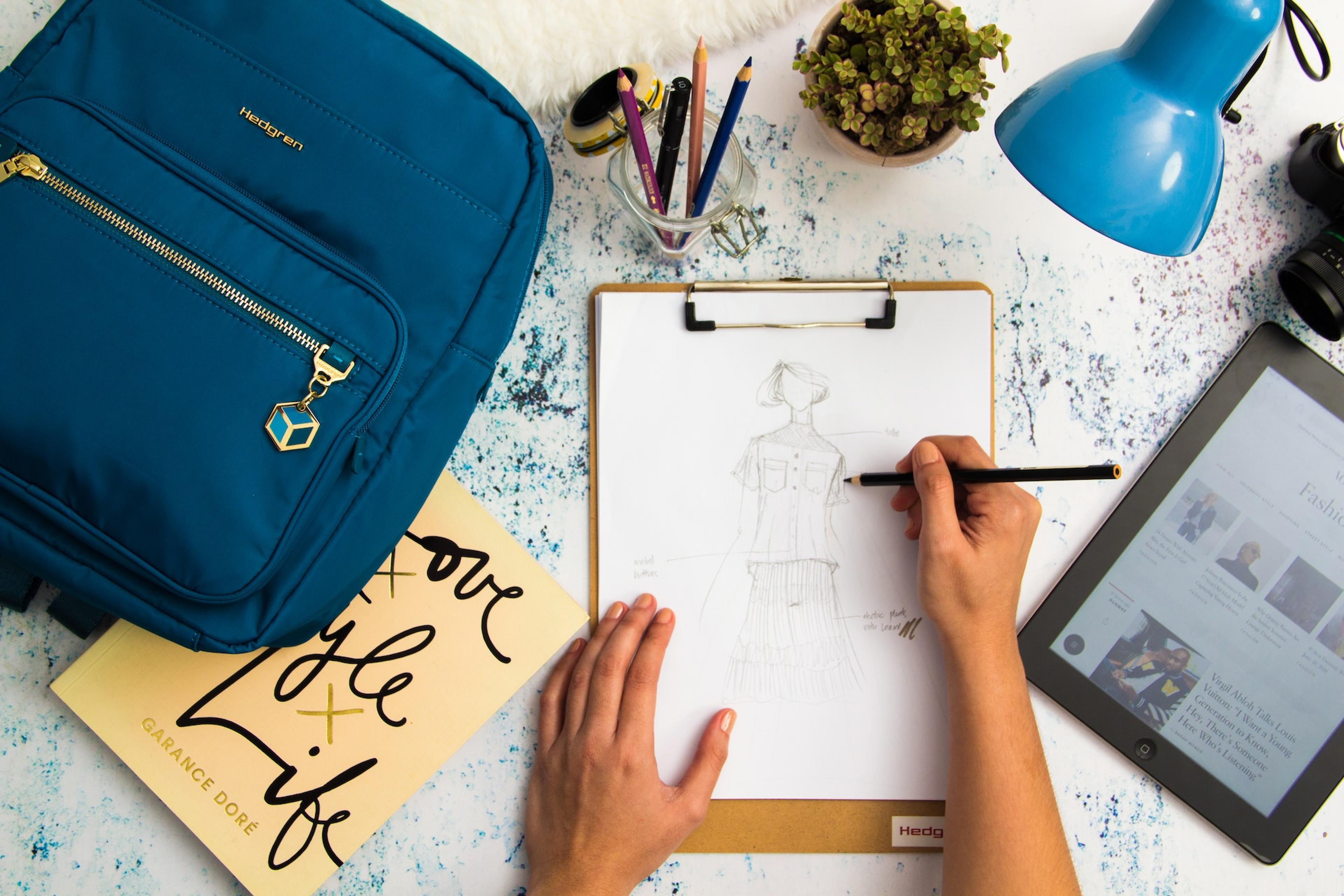 A pair of hands draws a fashion design on a piece of white paper on a clipboard