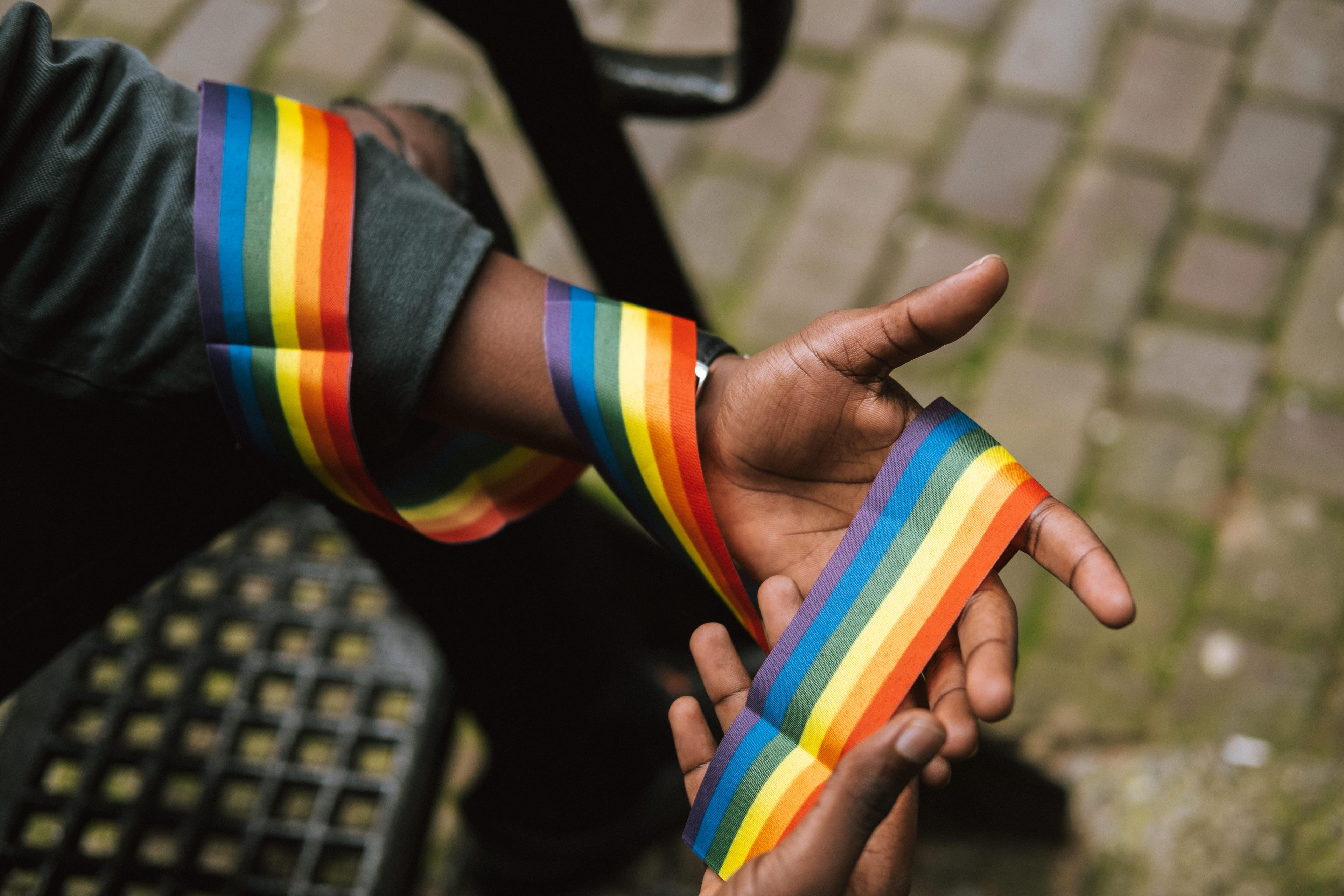 A Black person's arm and hand, wrapped in a rainbow ribbon