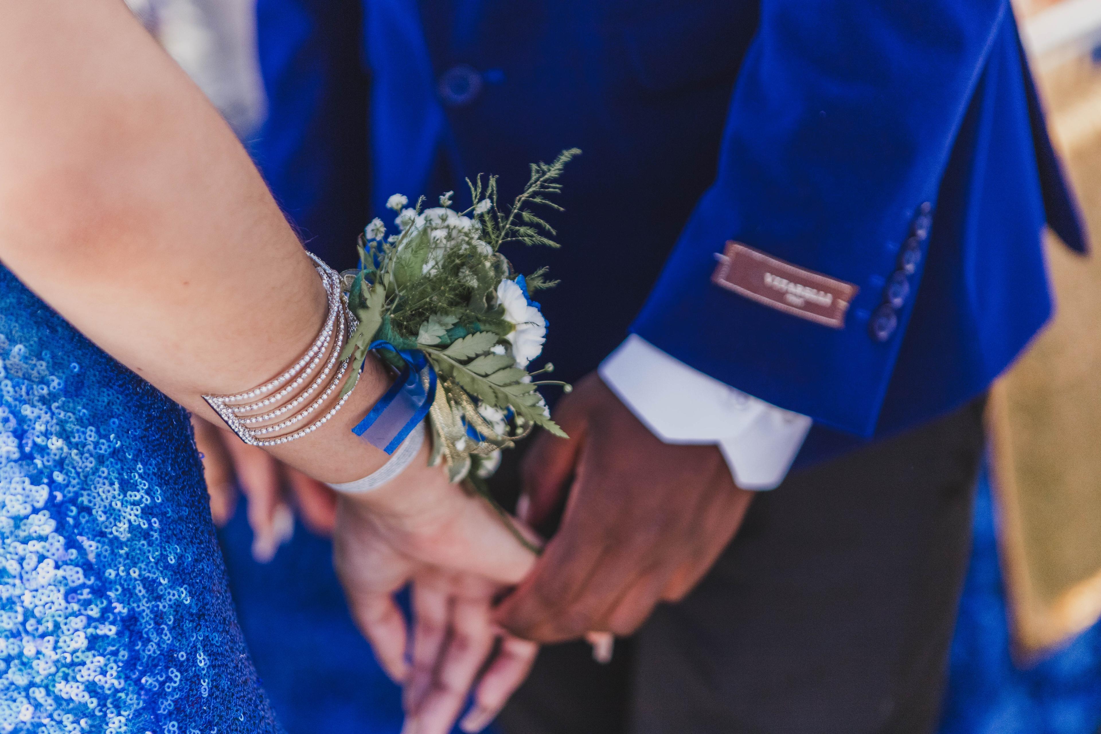 A shot of a man and woman people holding hands, both wearing blue and dressed up for prom