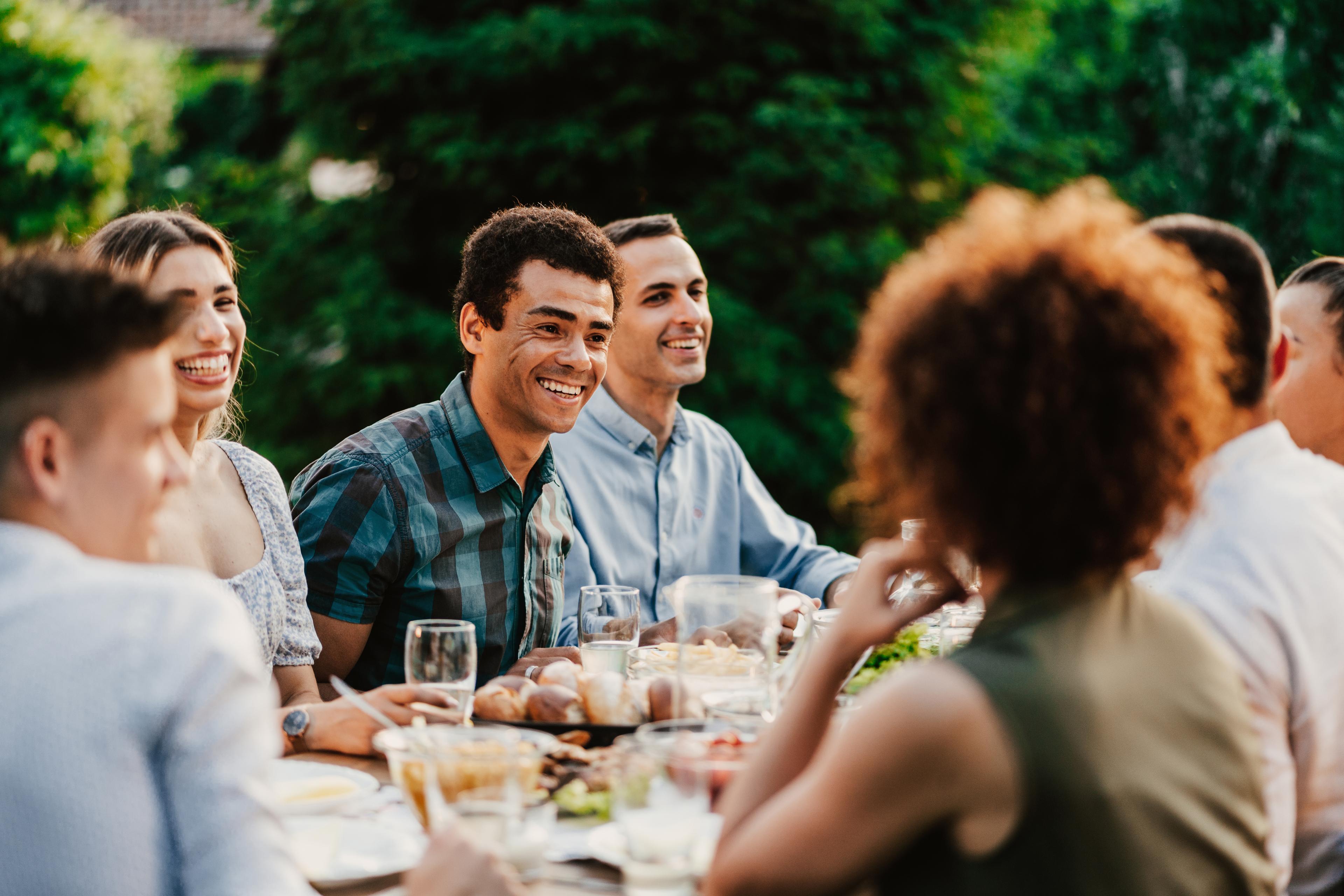 Group of adults smiling and gathering around a table outside