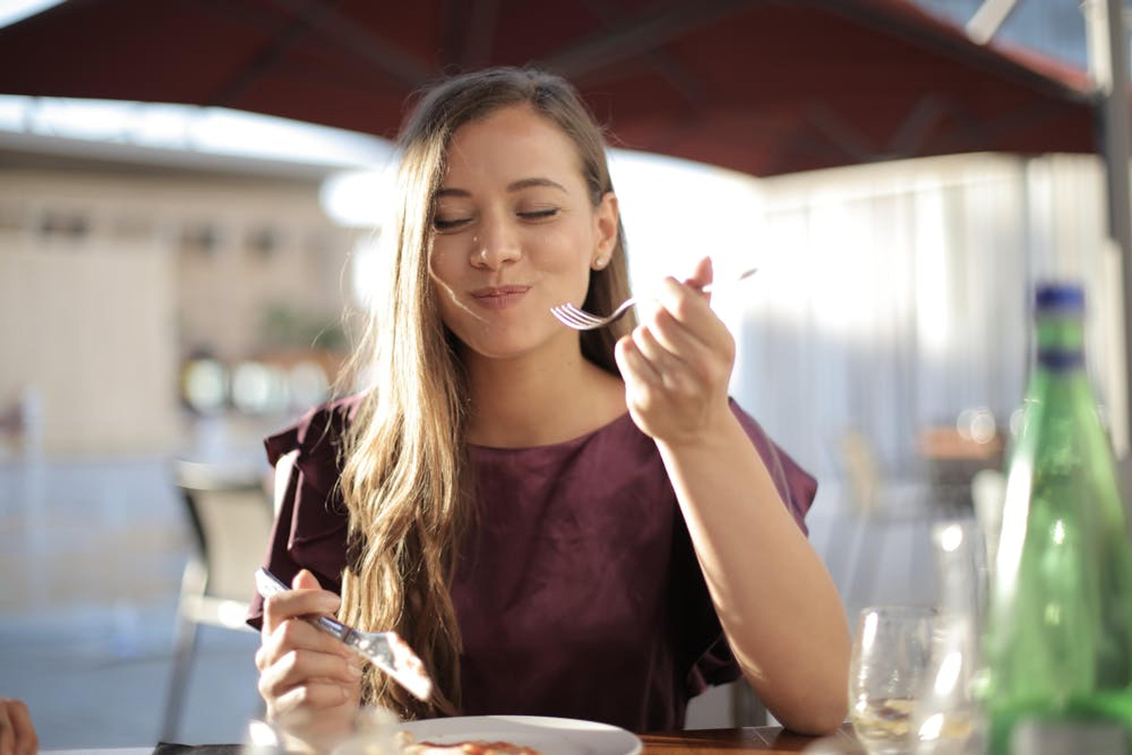 A smiling woman at an outdoor restaurant eats a bite of food