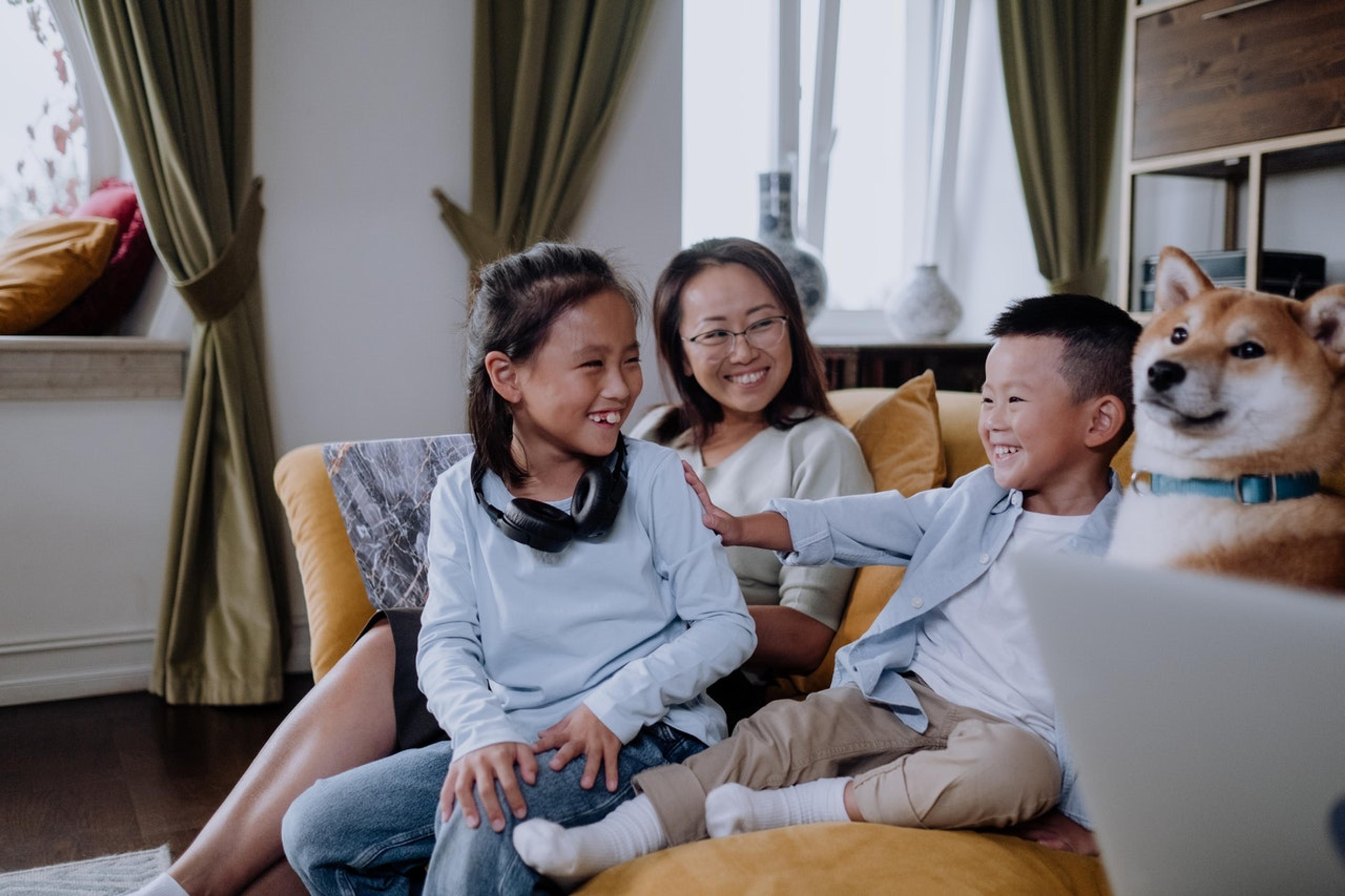 A mother and two children sit with their dog on a couch, laughing