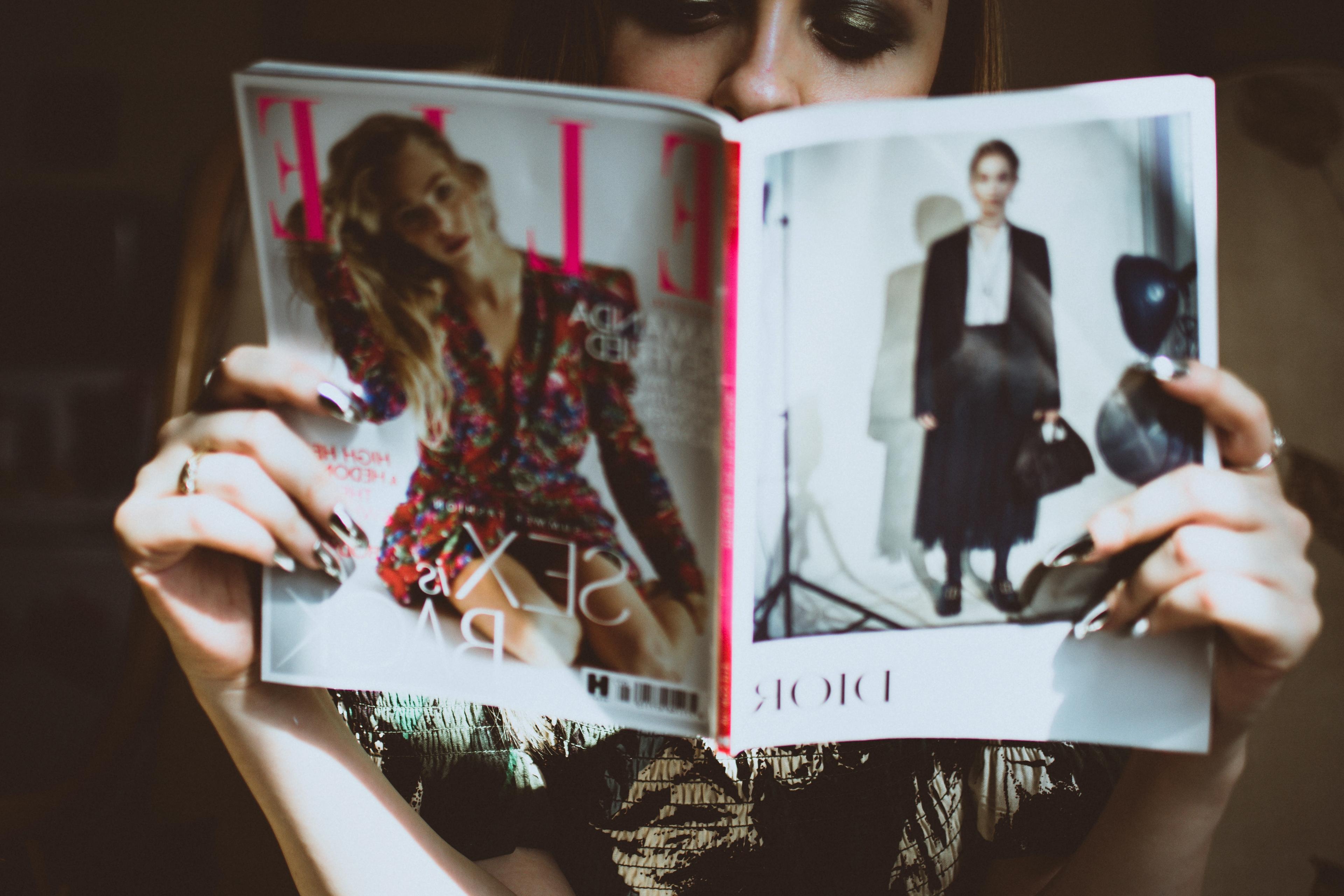 A woman reading a fashion magazine held up to obscure most of her face