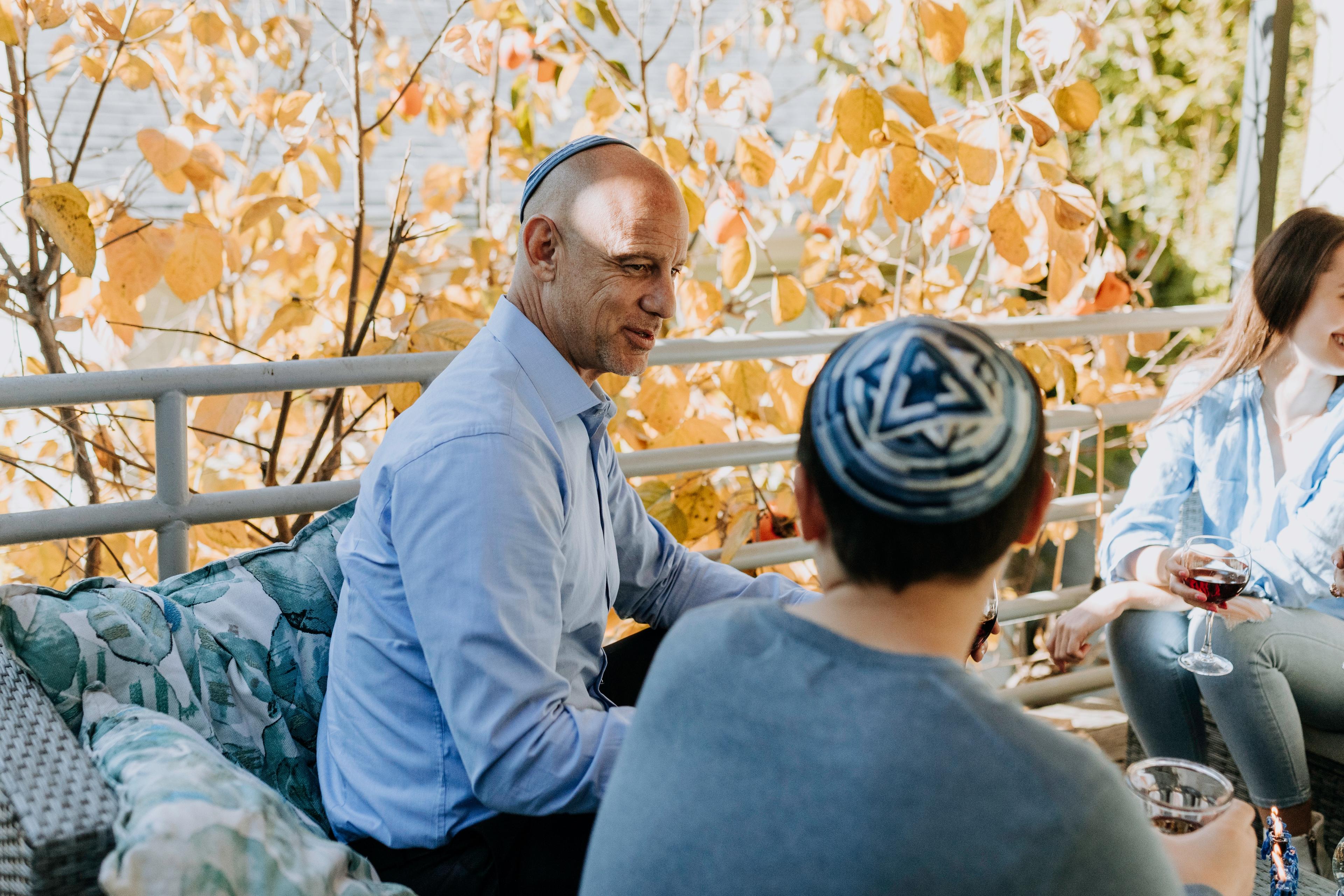 A man and a young boy, both wearing yarmulkes, talk to one another on an outdoor deck