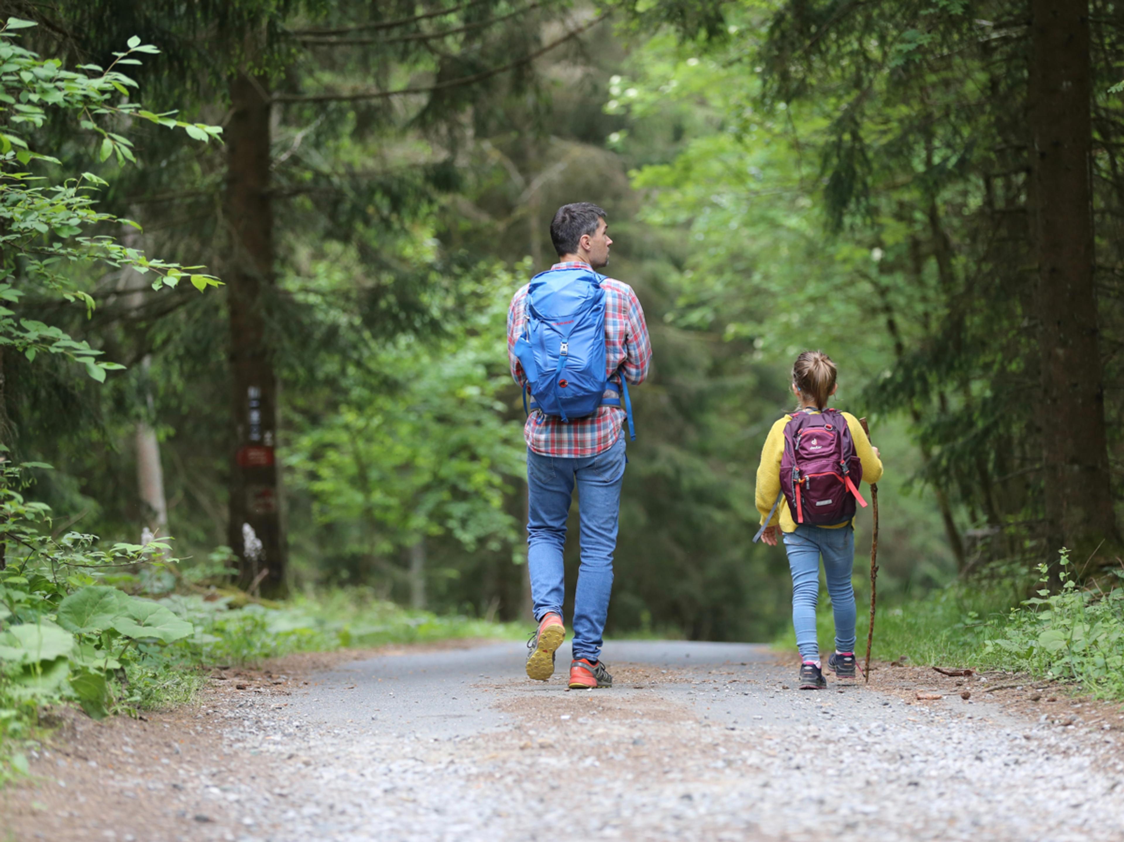 A man and young girl walk together in the woods wearing hiking backpacks