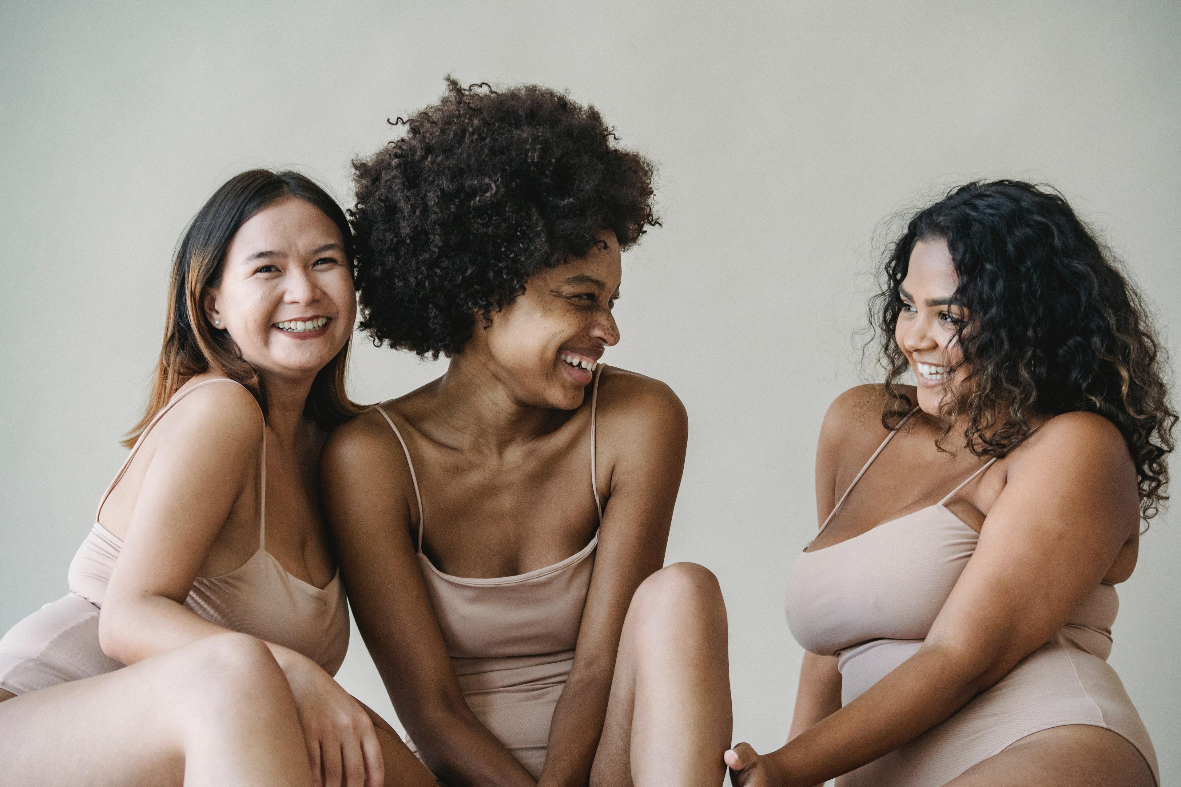 Three women with different skin tones smiling at each other