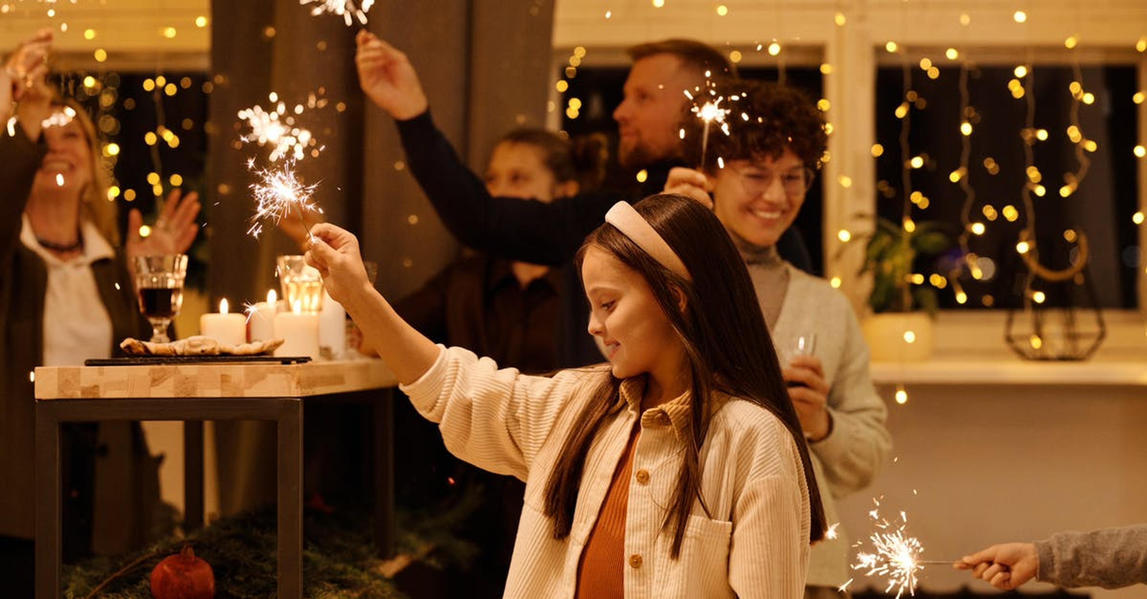 A young girl holds up a sparkler at a New Year's Eve party