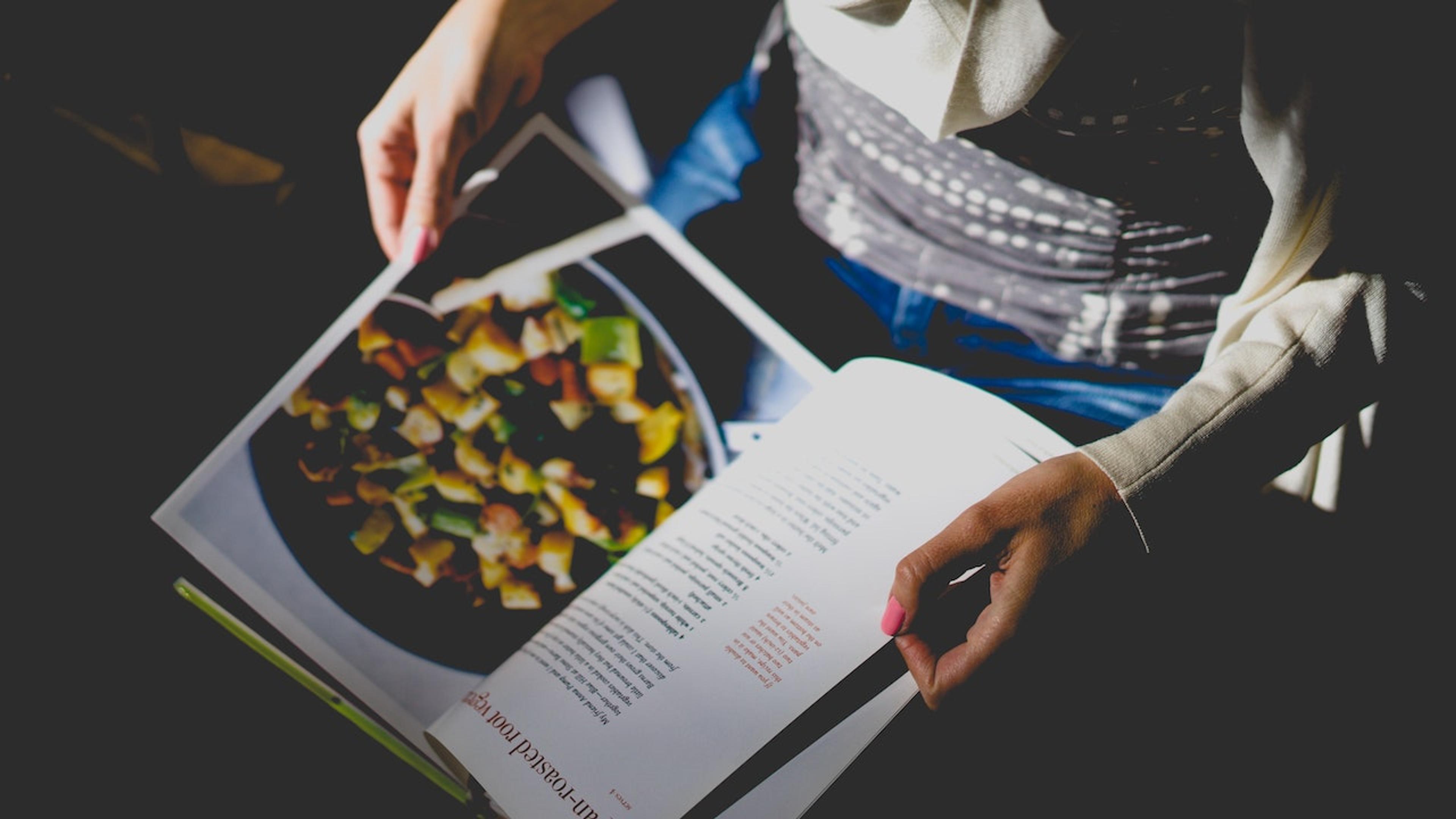 A person holds open a cookbook, looking at a recipe