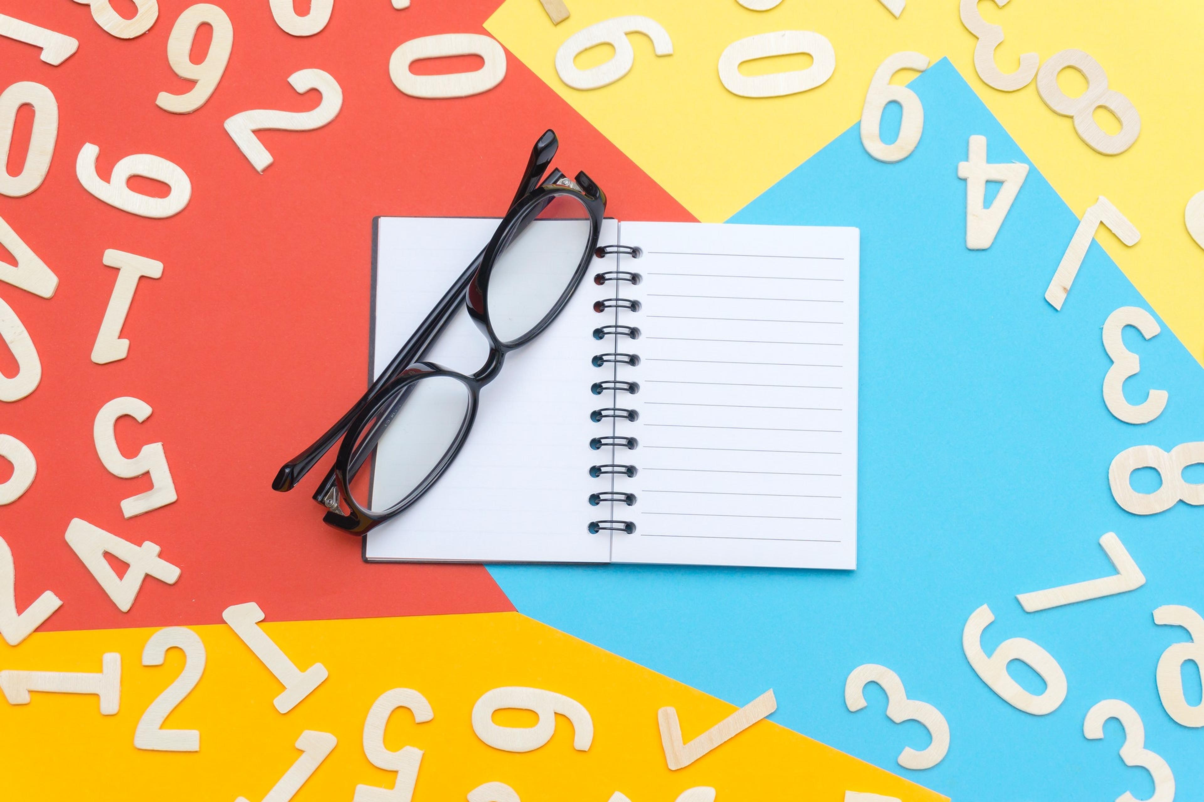 Glasses and a blank notebook on a colorful background with numbers around it