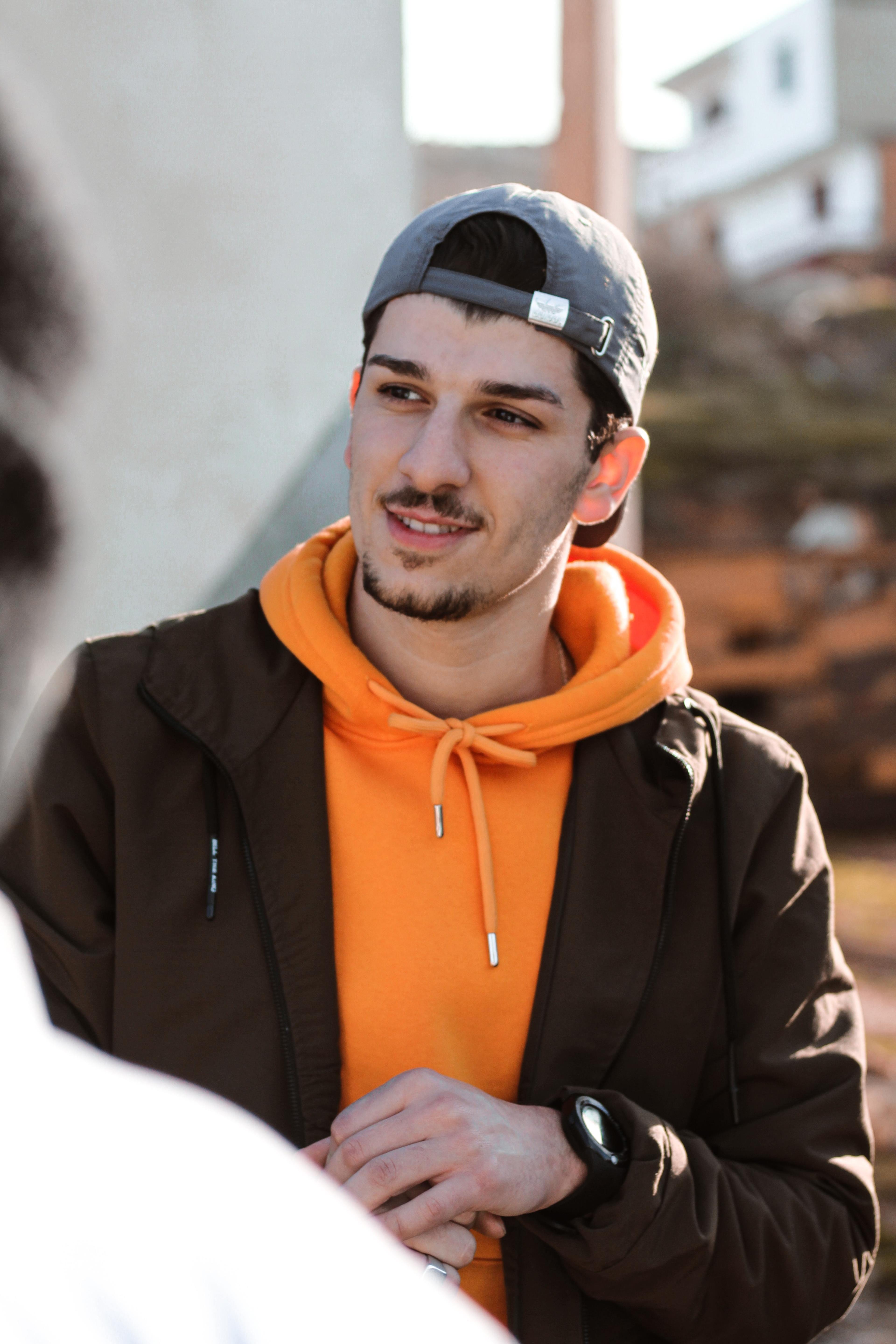 A young man in an orange hoodie and backwards cap