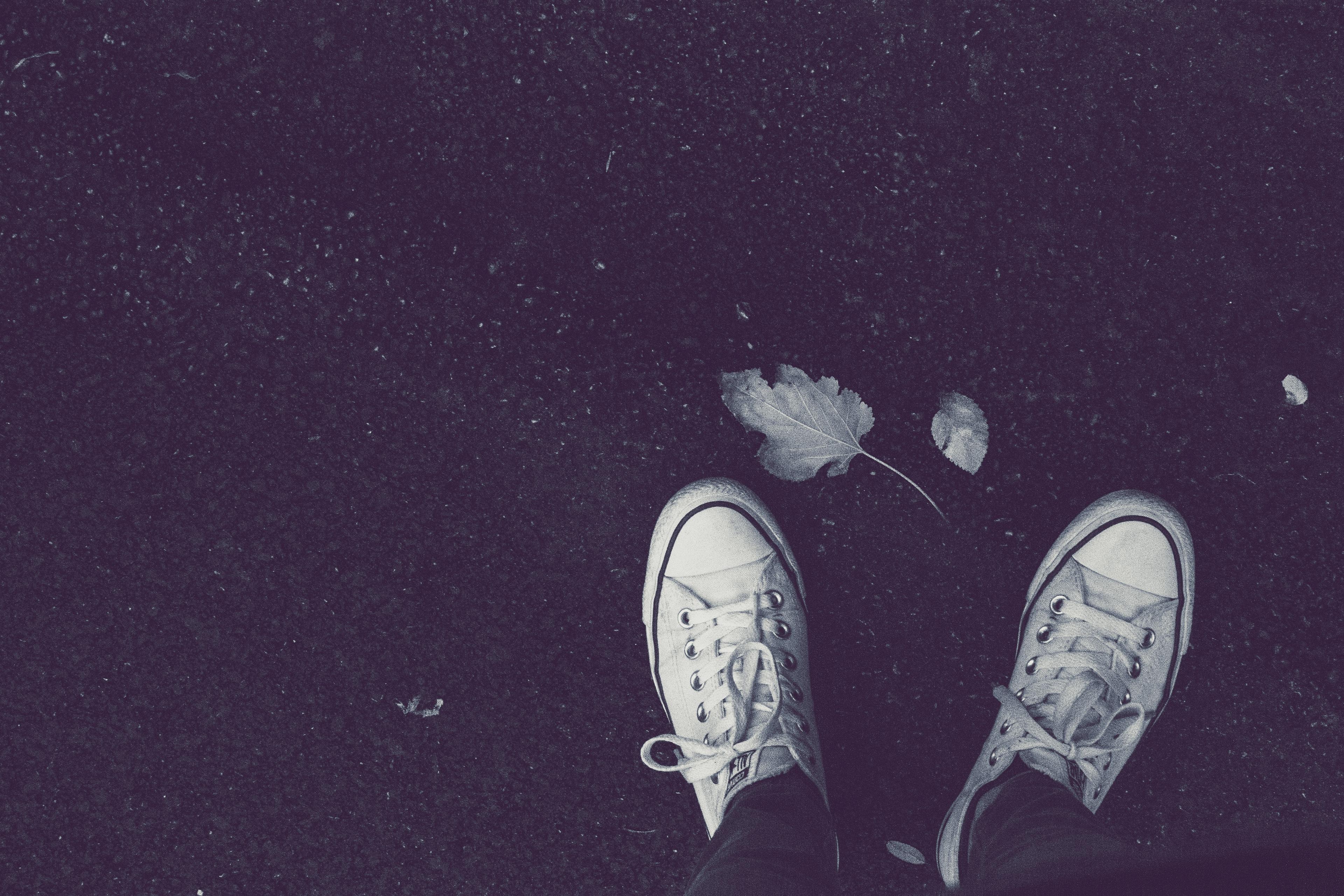 A black and white photo of someone standing in white shoes on black ground