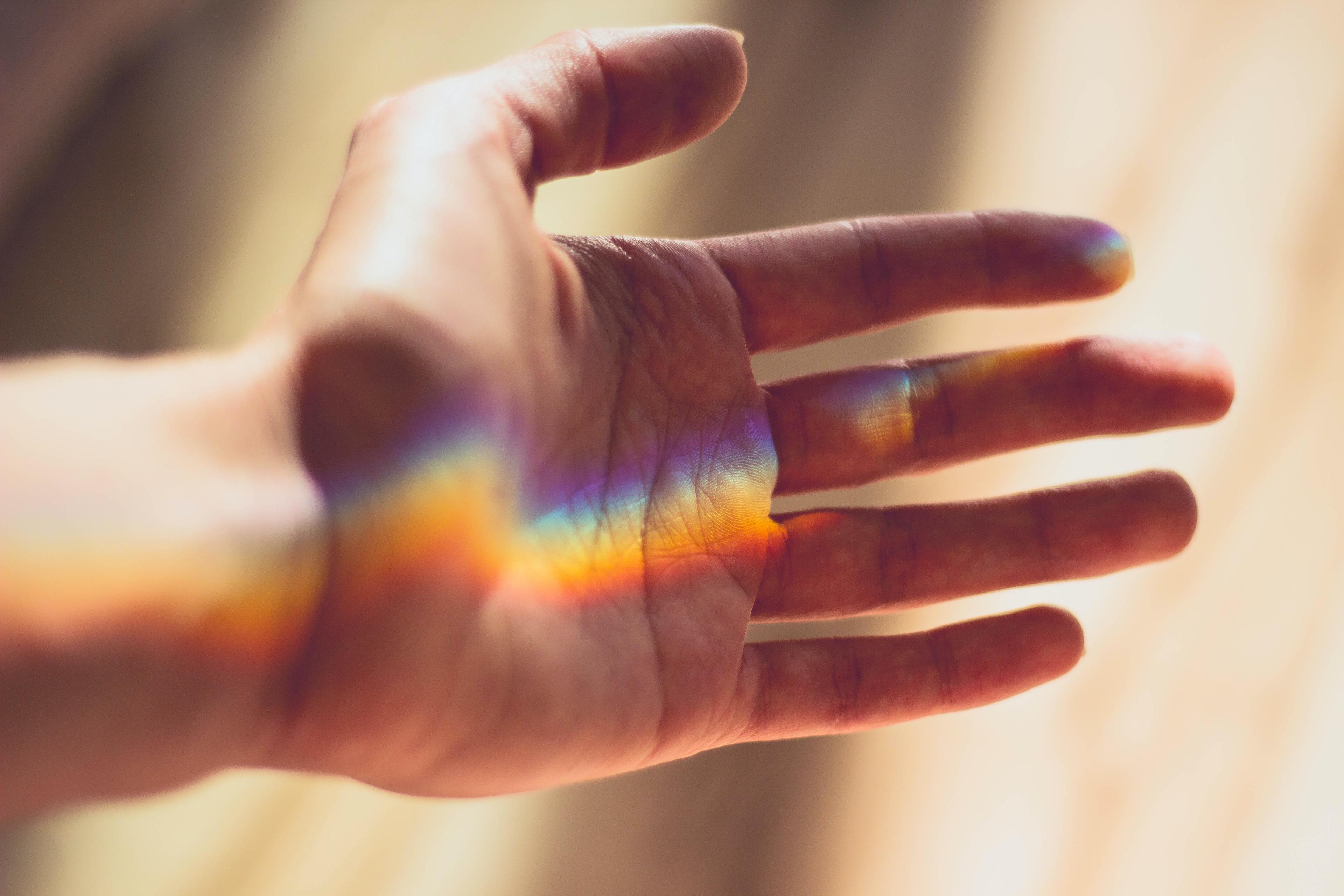 A hand in the sun with a reflected rainbow light across the palm