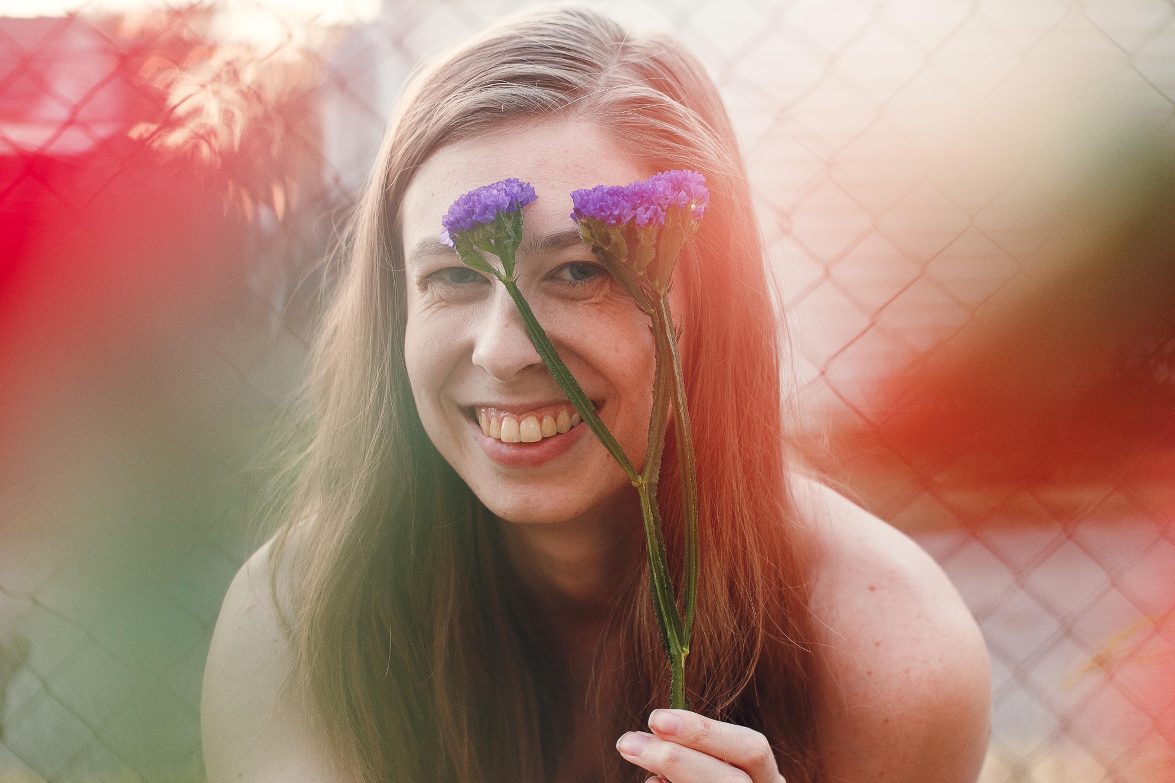 A smiling woman holds a flower up to her face
