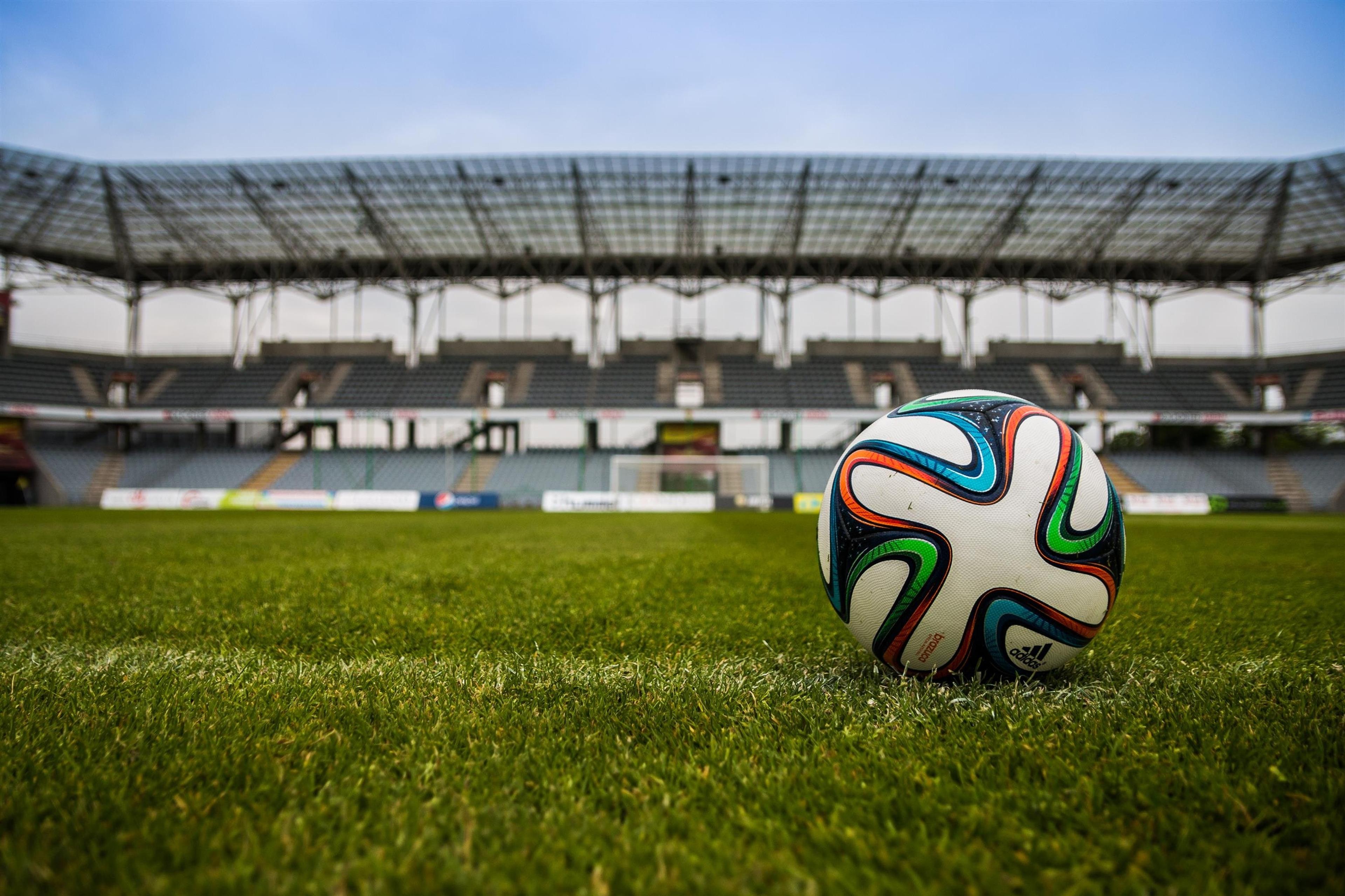 A colorful soccer ball rests on turf on an empty soccer field
