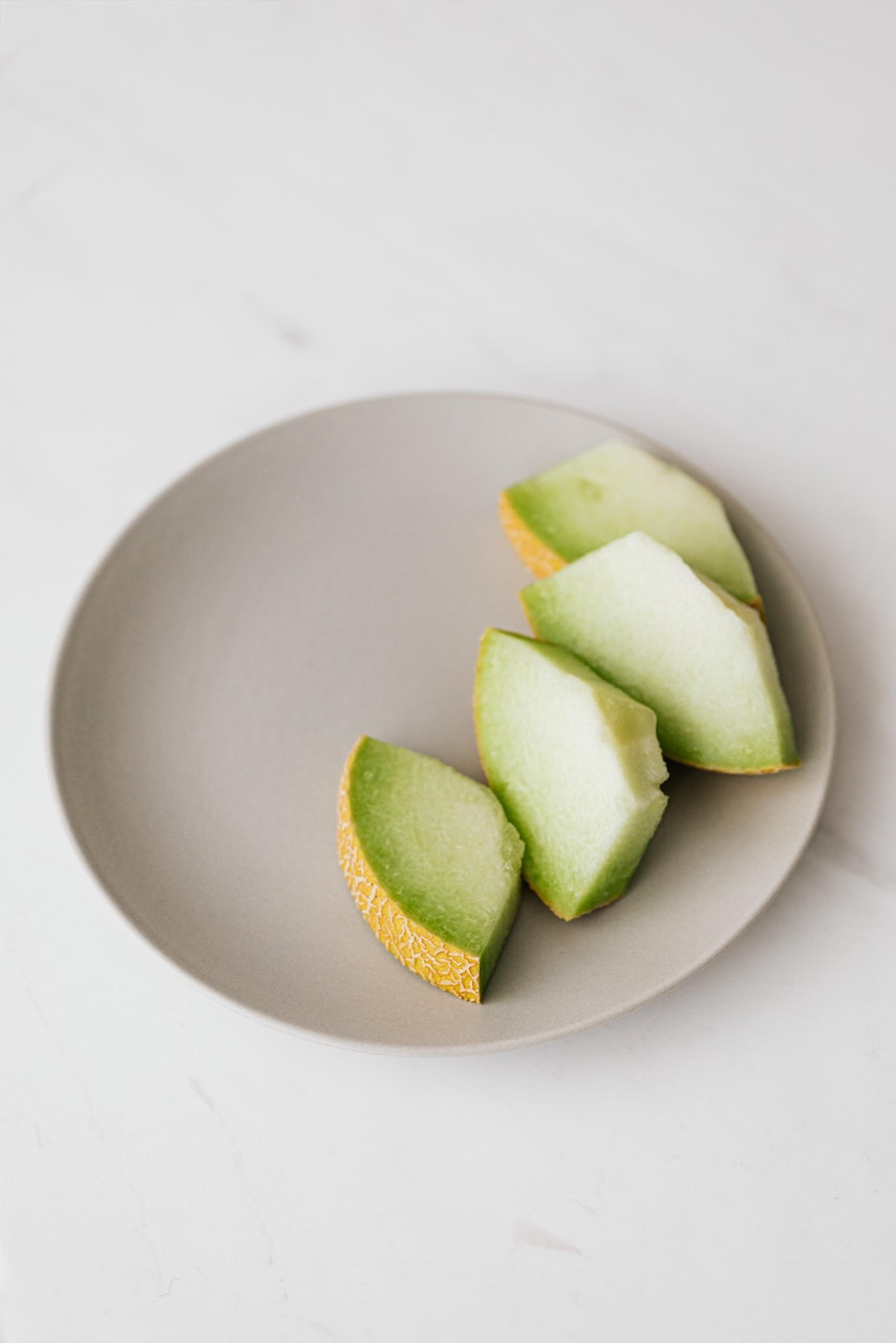 A gray plate with some slices of honeydew melon across part of it