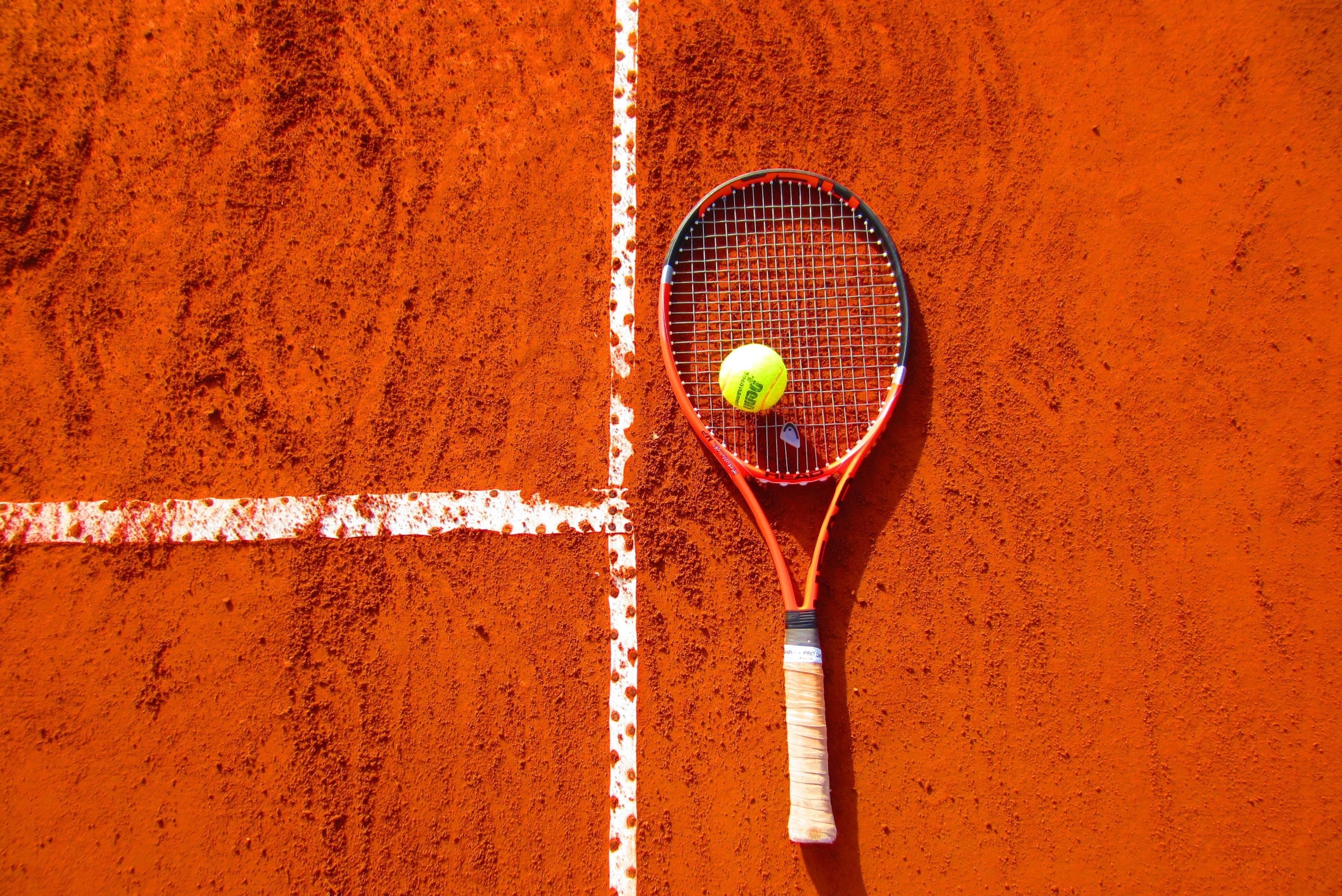 A tennis racket and tennis ball on an orange-red background