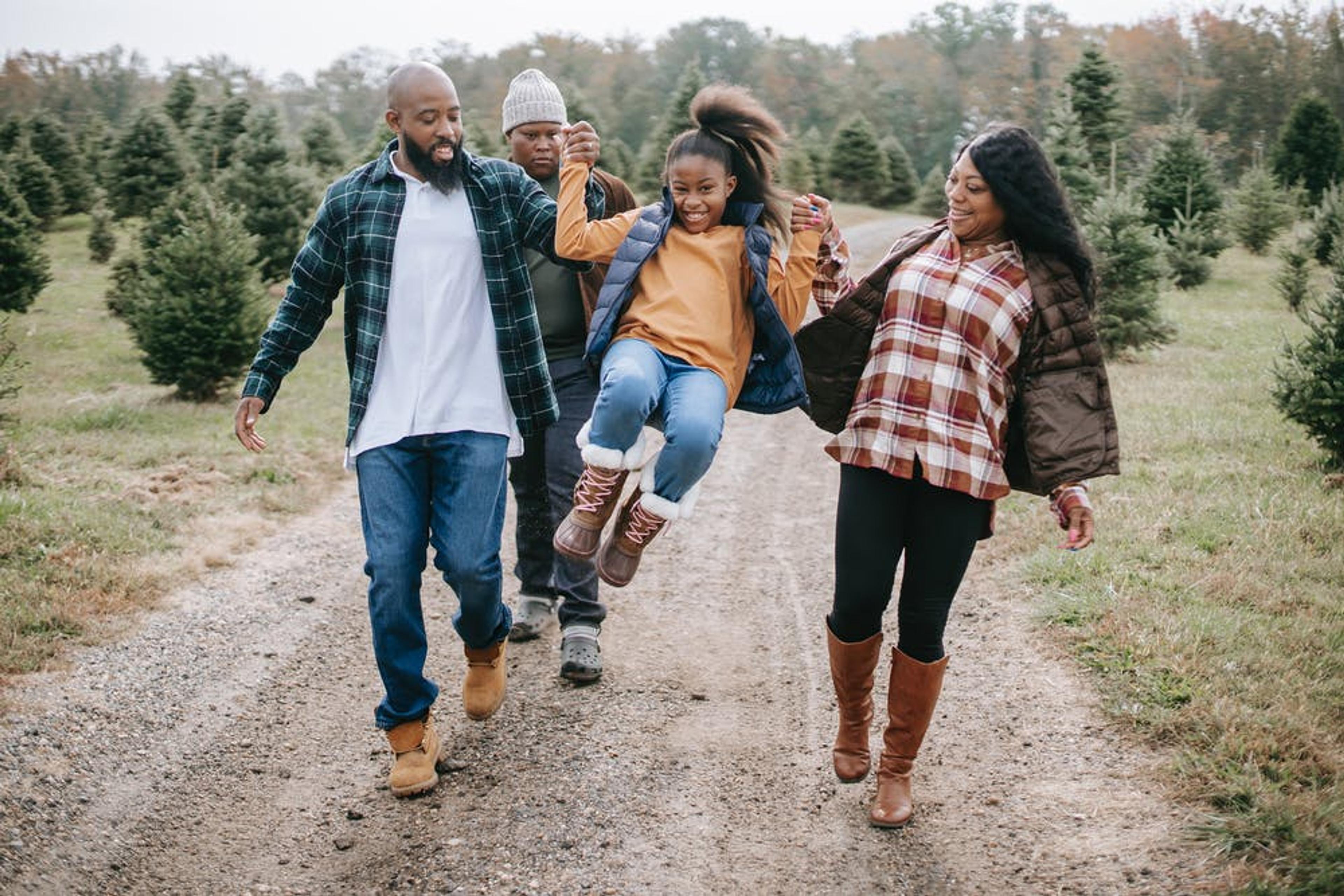 Two parents swing their daughter between them as they walk through a Christmas tree farm