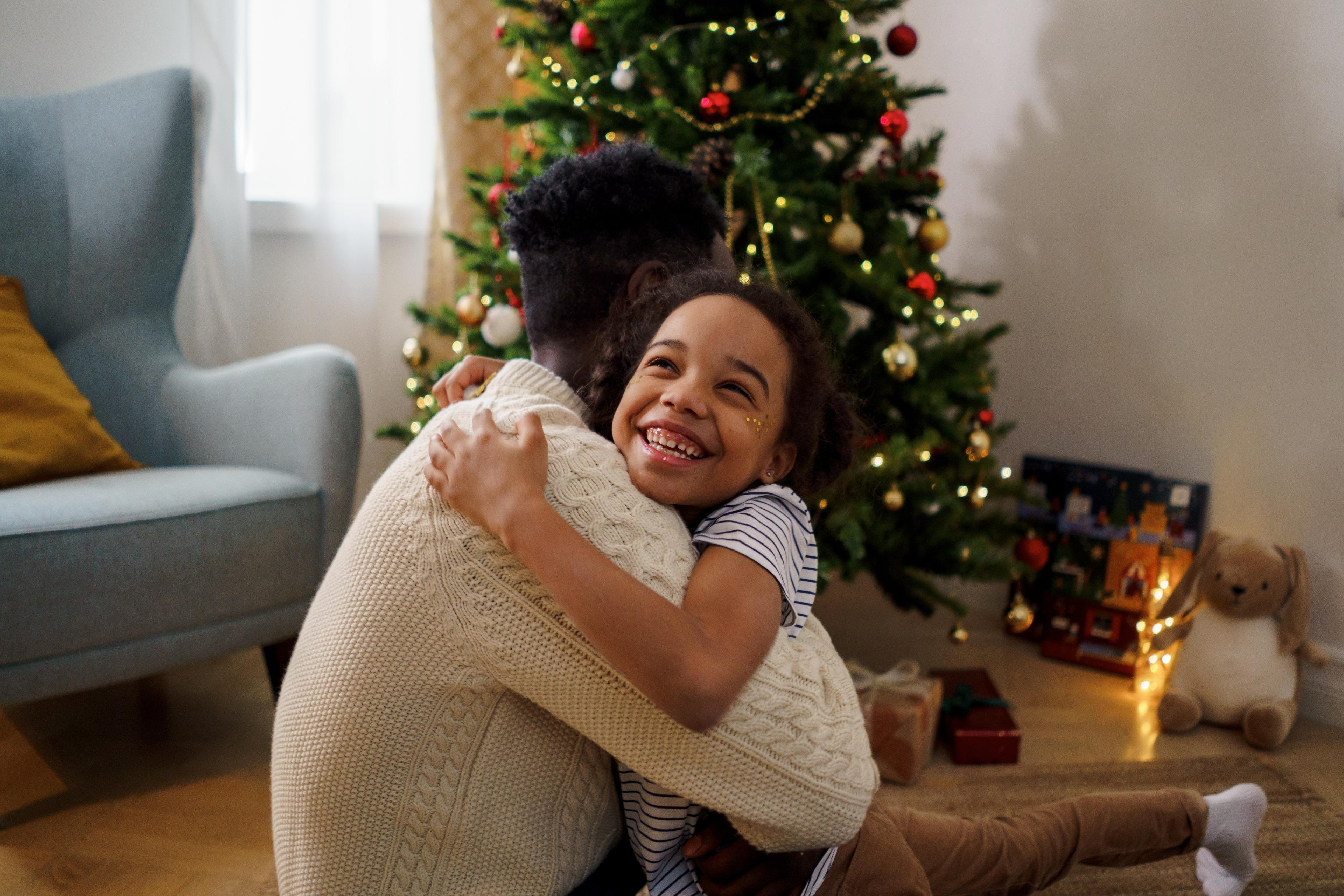 A young girl hugs her father in front of a Christmas tree