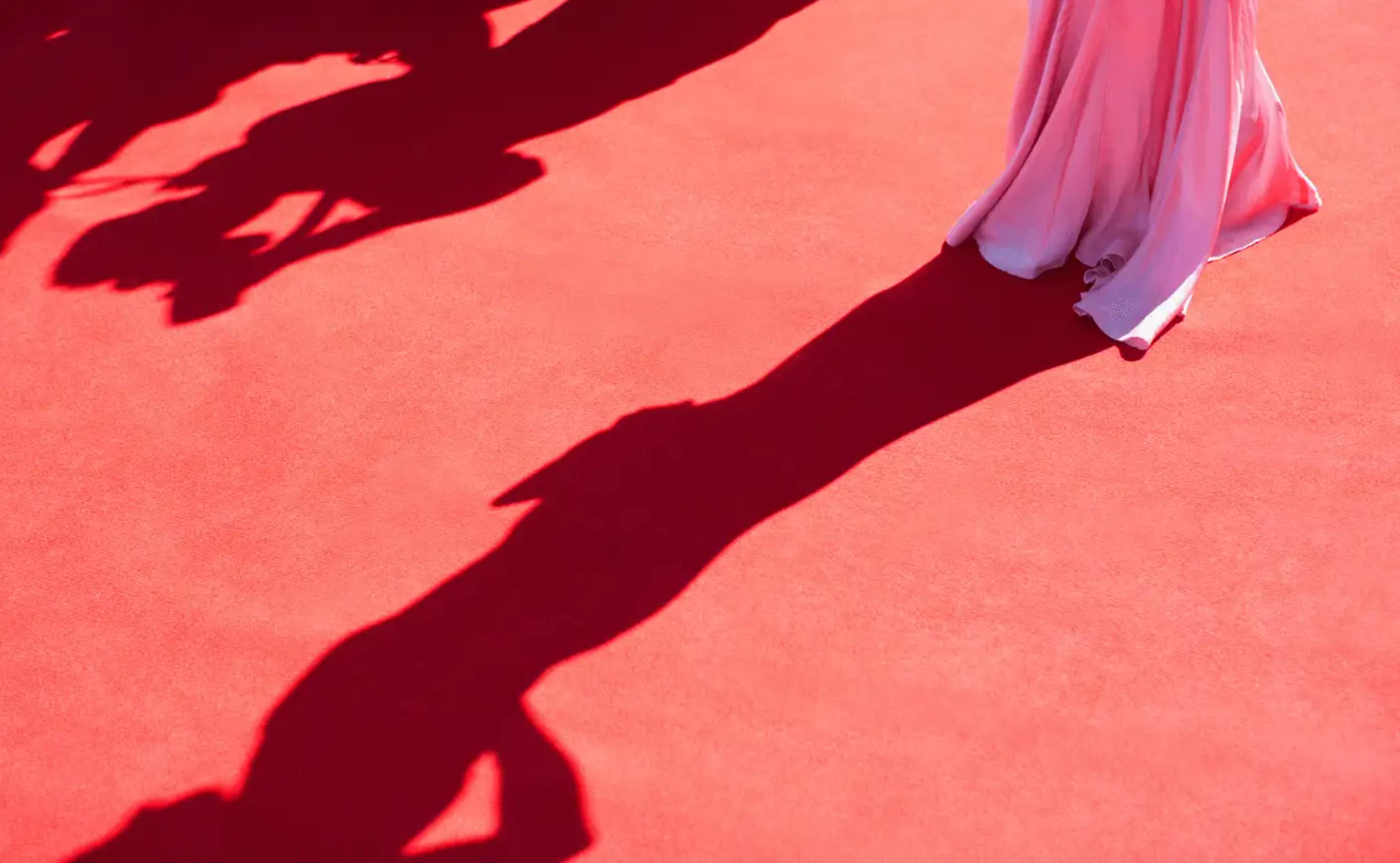 The bottom half of a woman in a pink gown on a red carpet