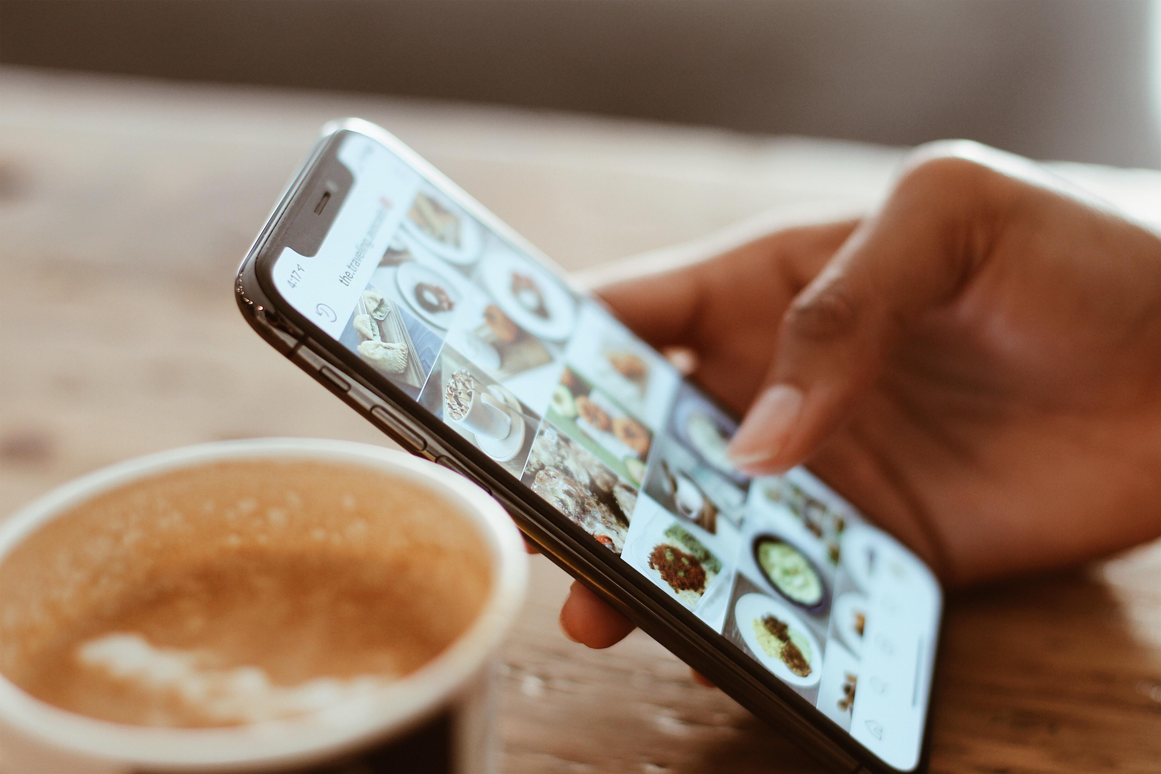 A hand scrolling social media on a smartphone, next to a cup of coffee