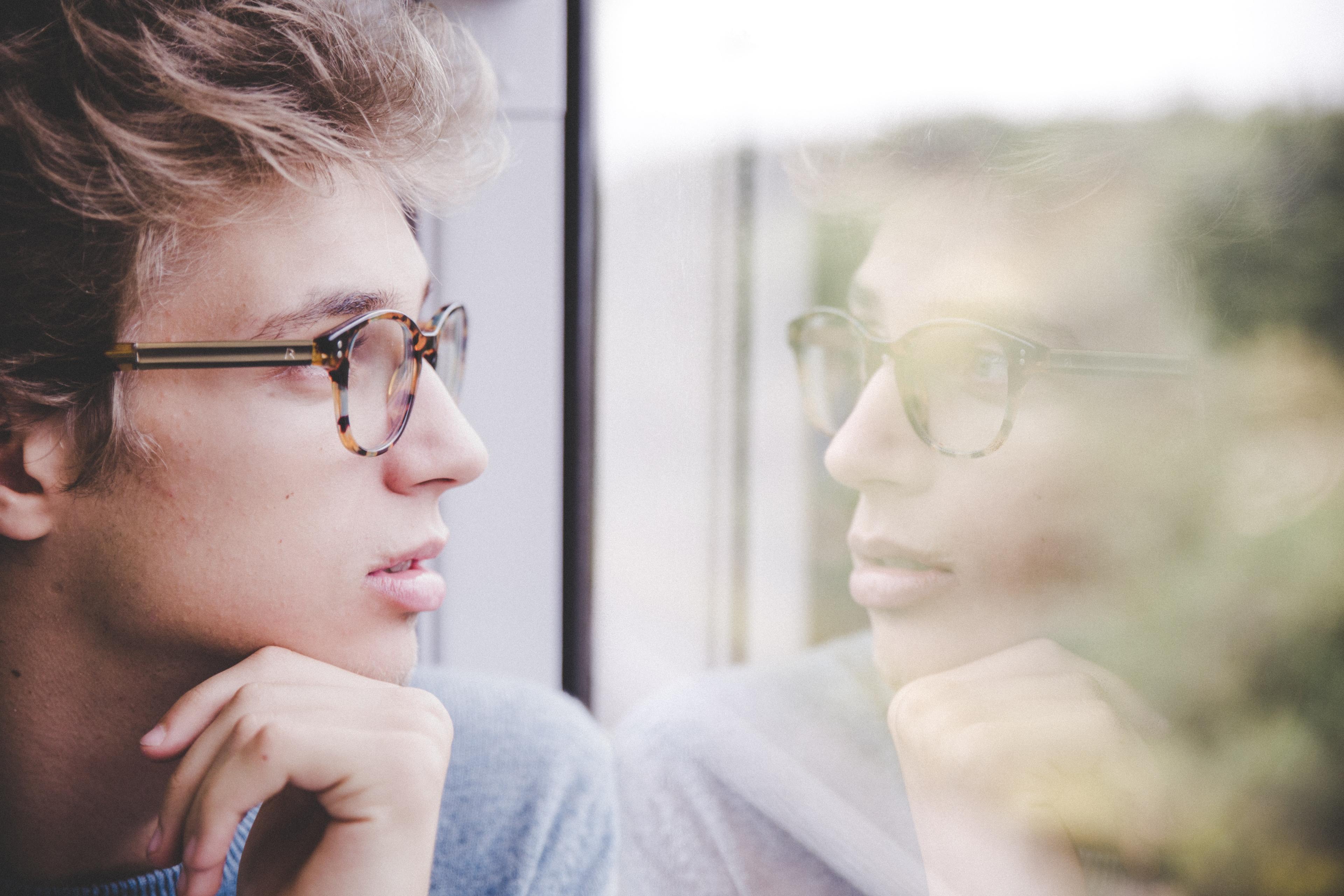 A young man looks at his reflection in the window