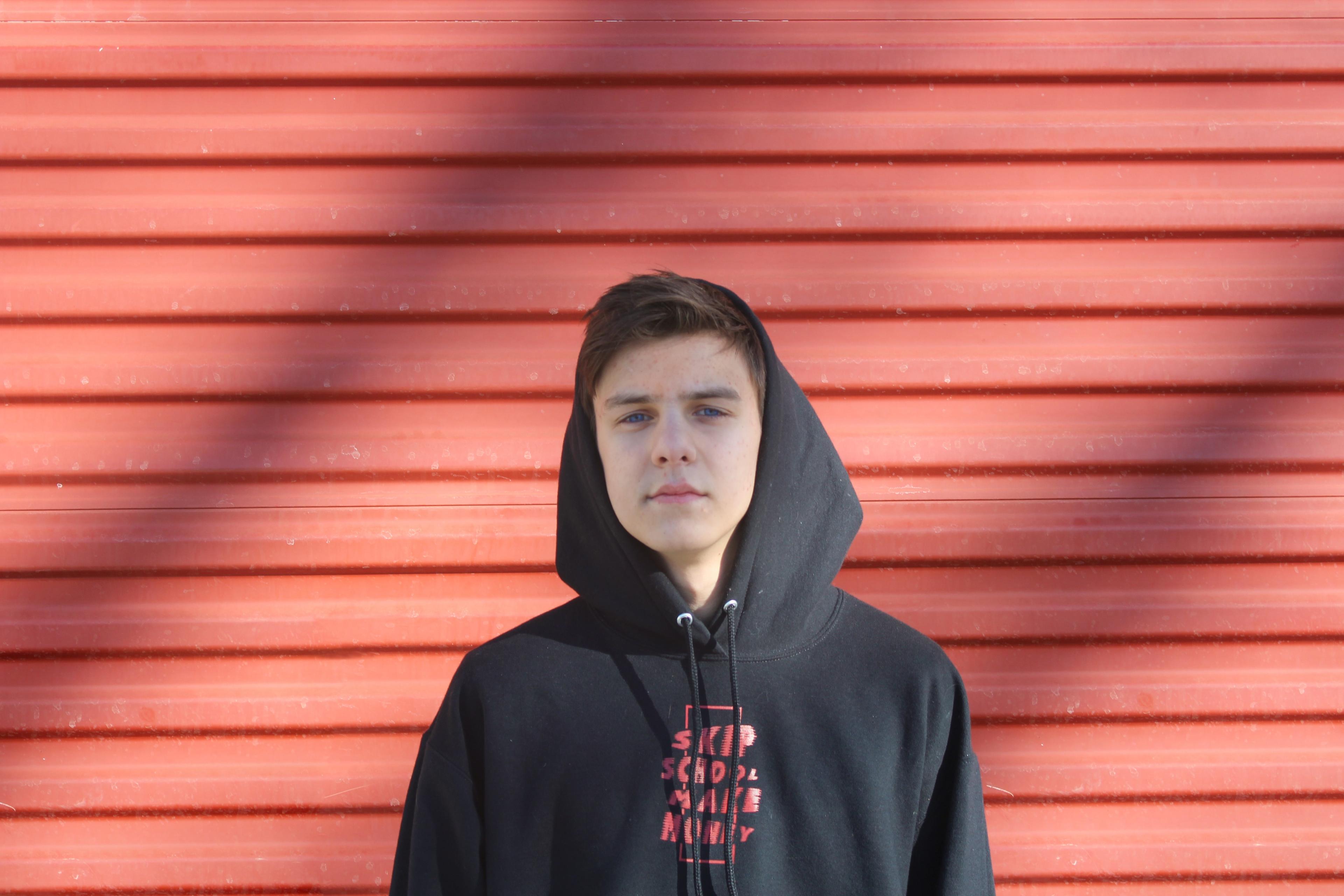A teenage boy in a black hoodie standing against a red wall