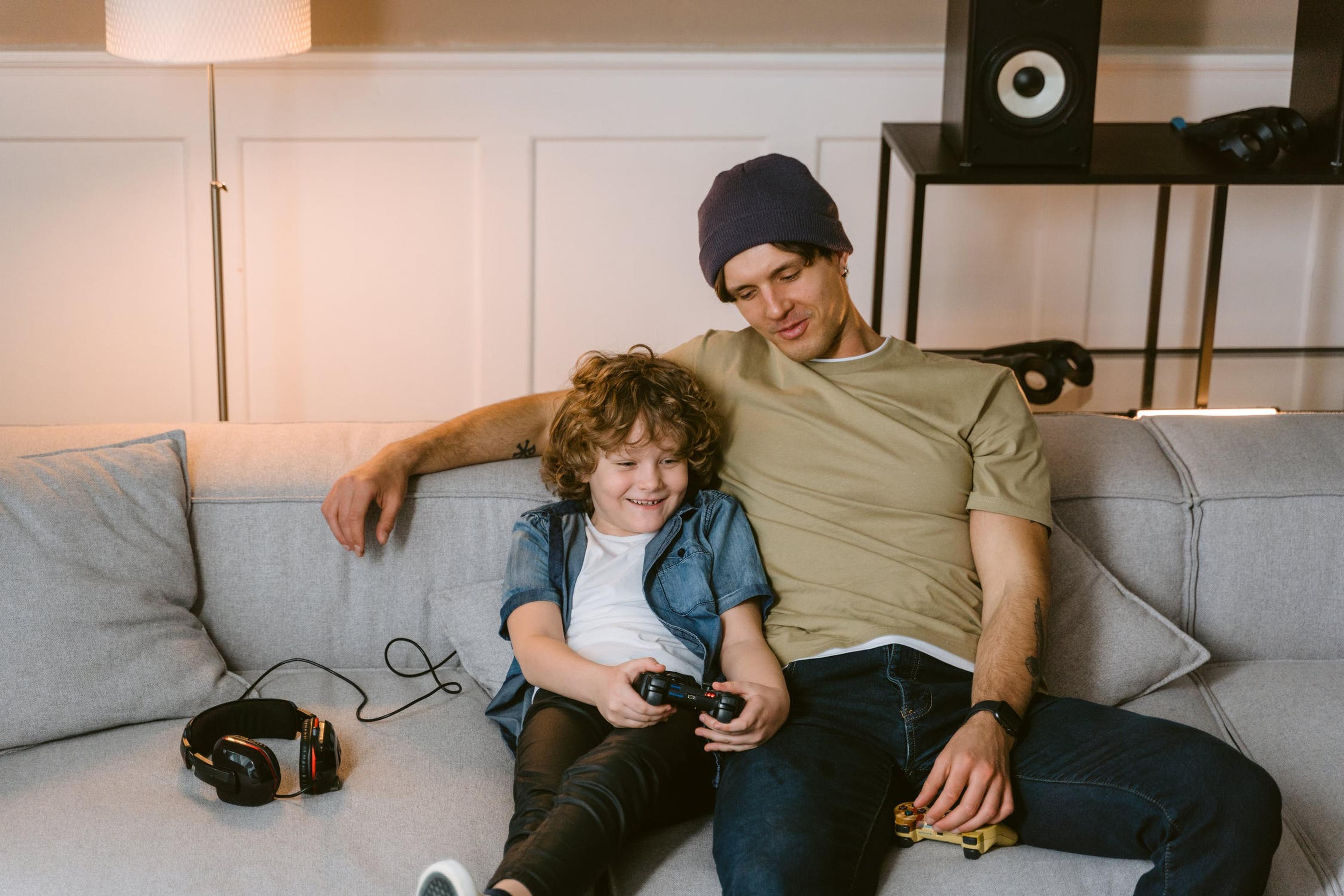 A father and son sit on a couch together playing video games