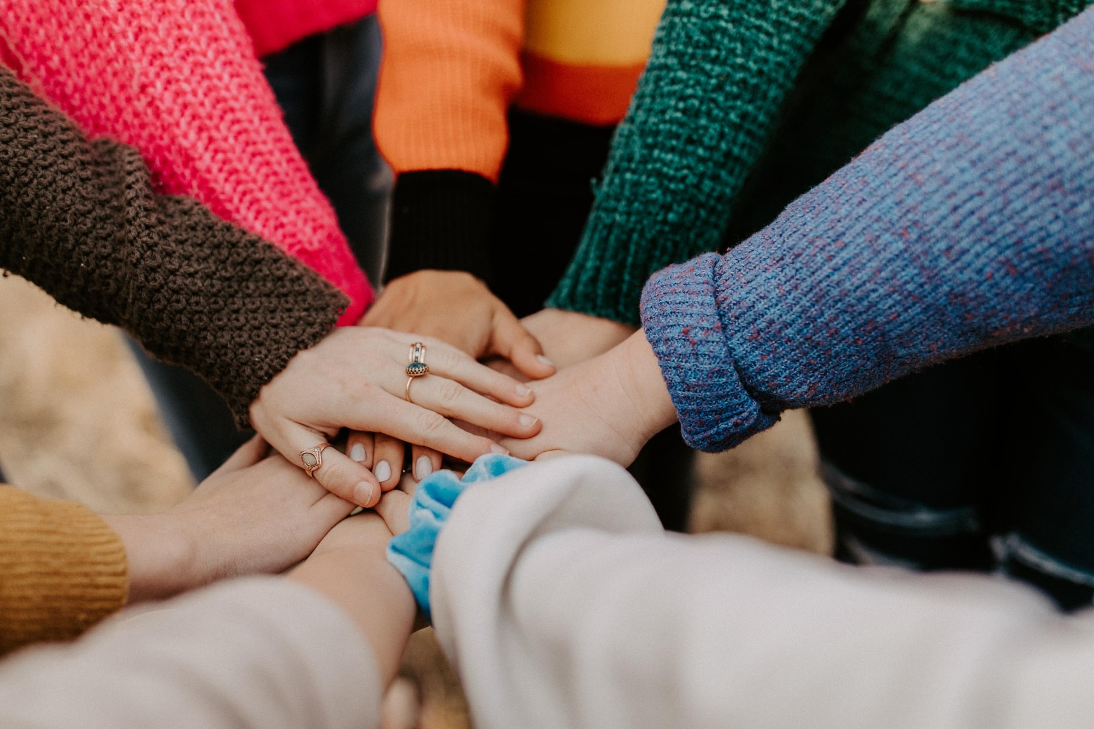 Young people in colorful sweaters put their hands in a circle