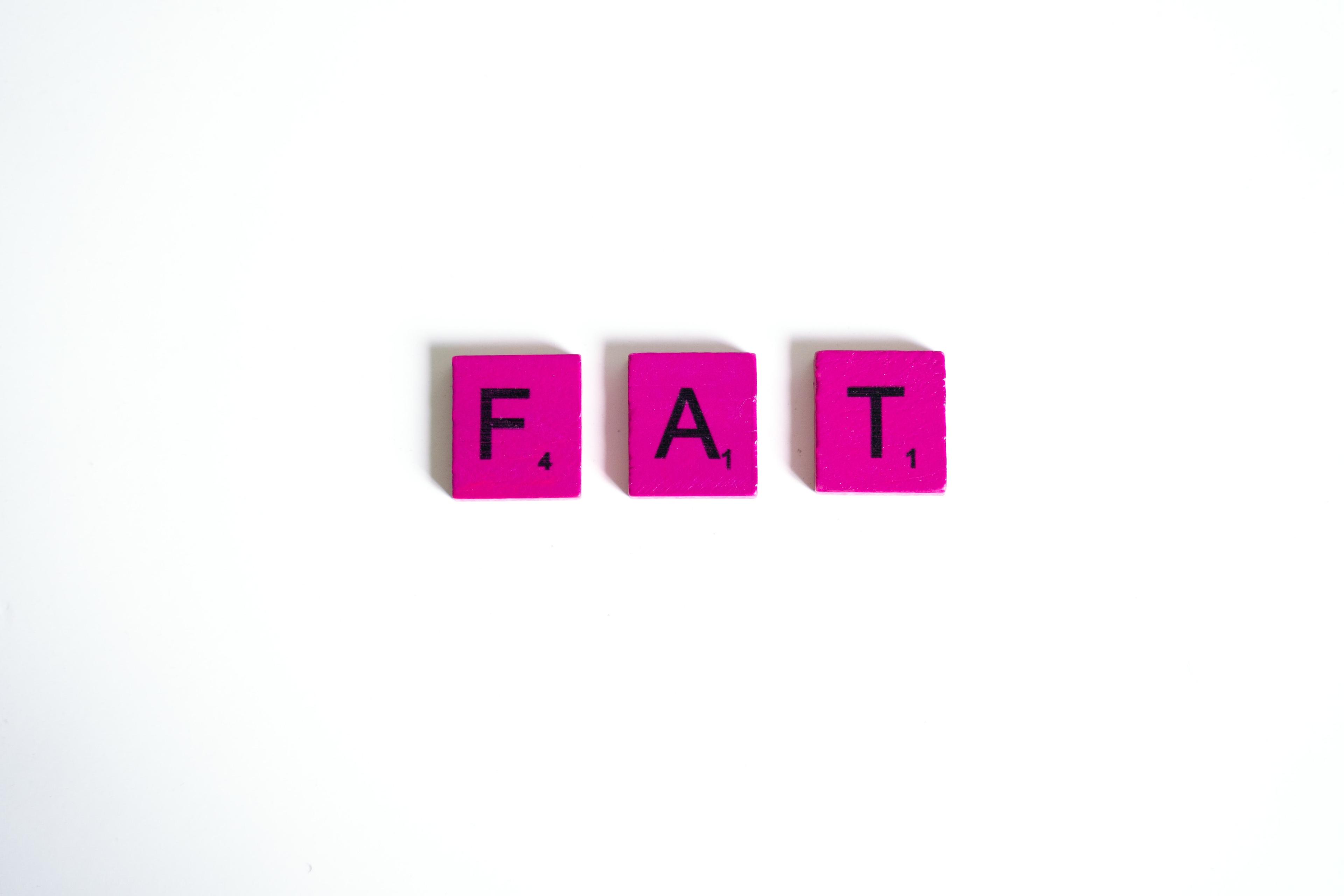 Pink Scrabble tiles spelling out the word "FAT" on a white background
