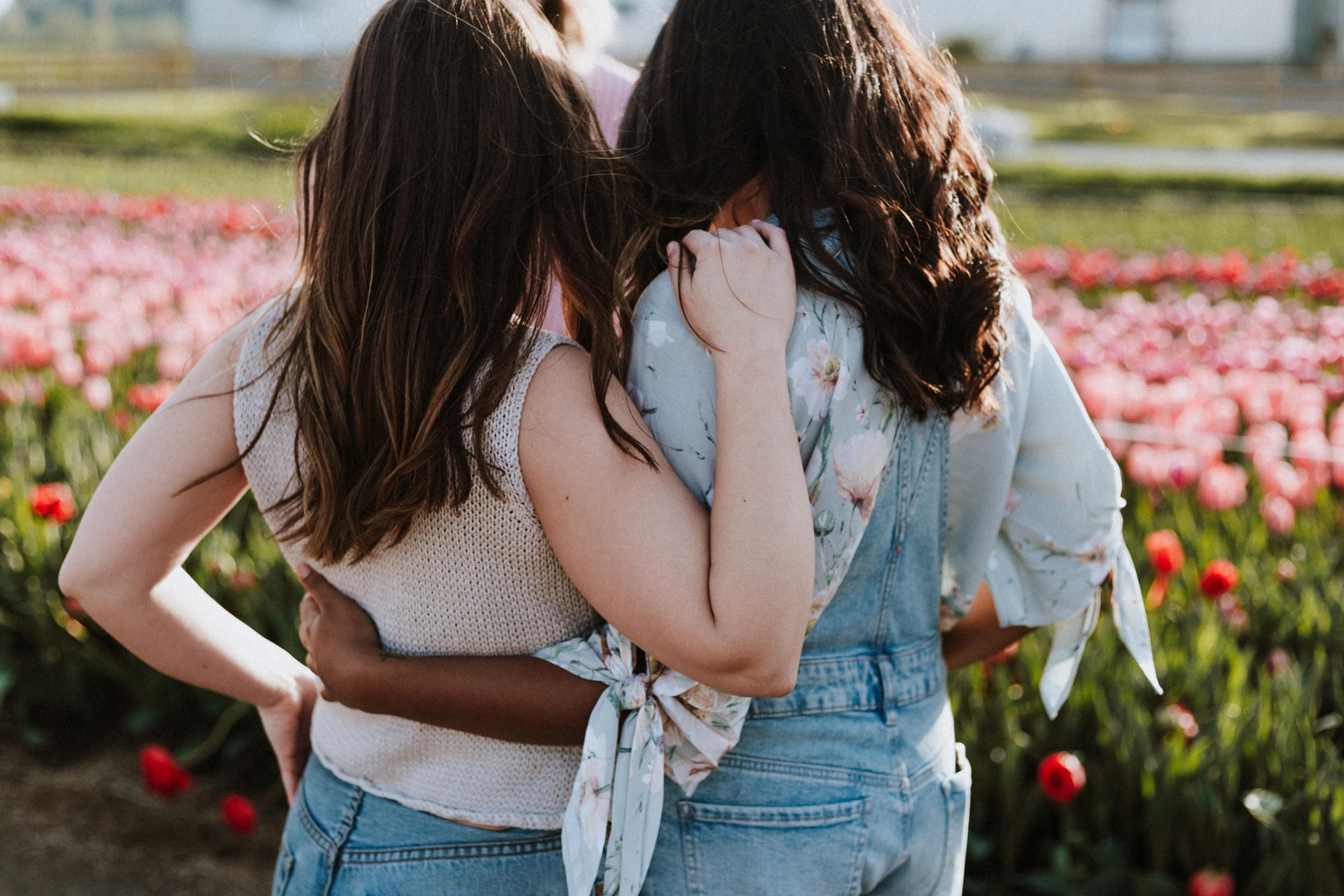 Two girls, backs to the camera, stand with their arms around each other looking out on a field of tulips