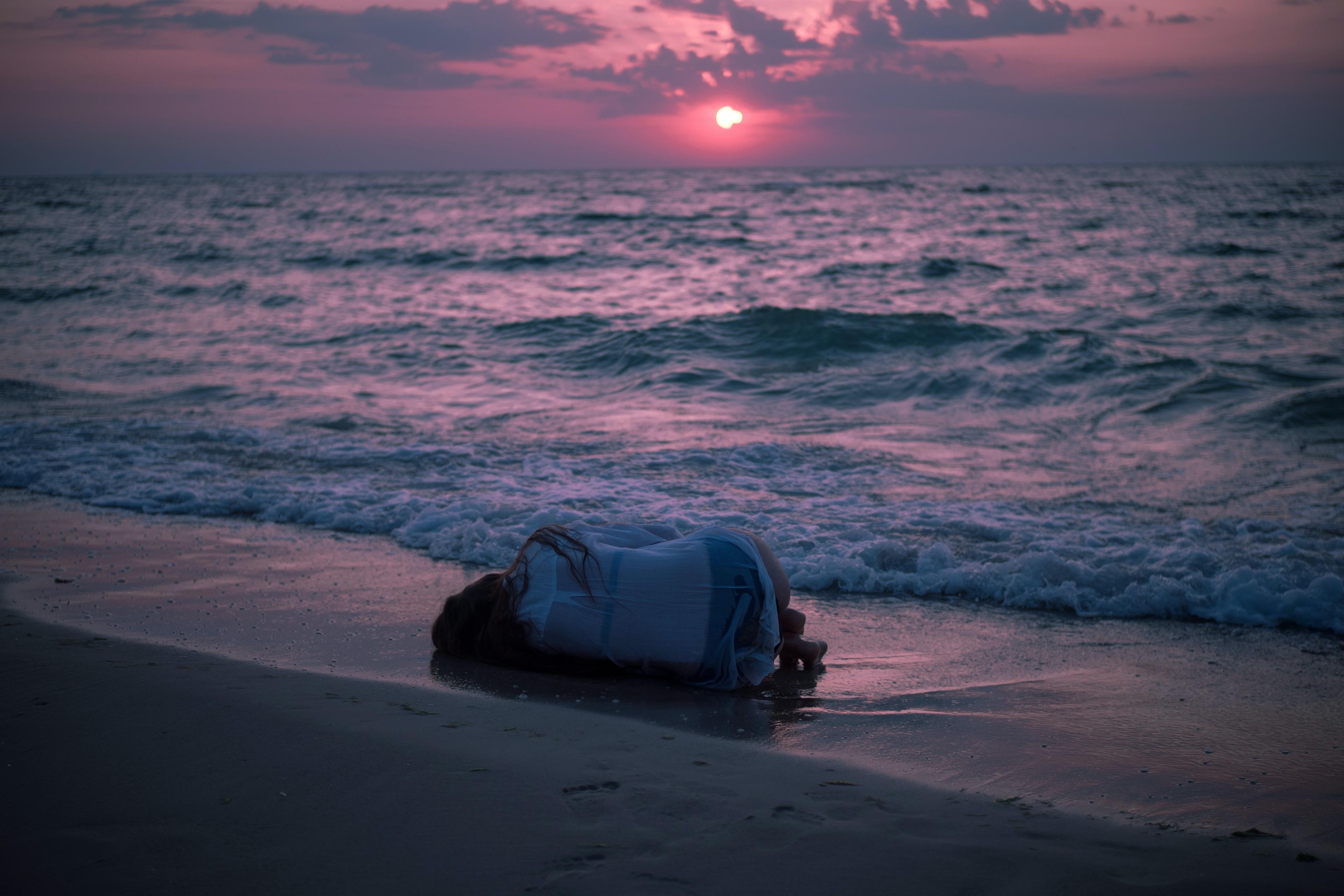 A woman lying in the fetal position on the beach at sunset