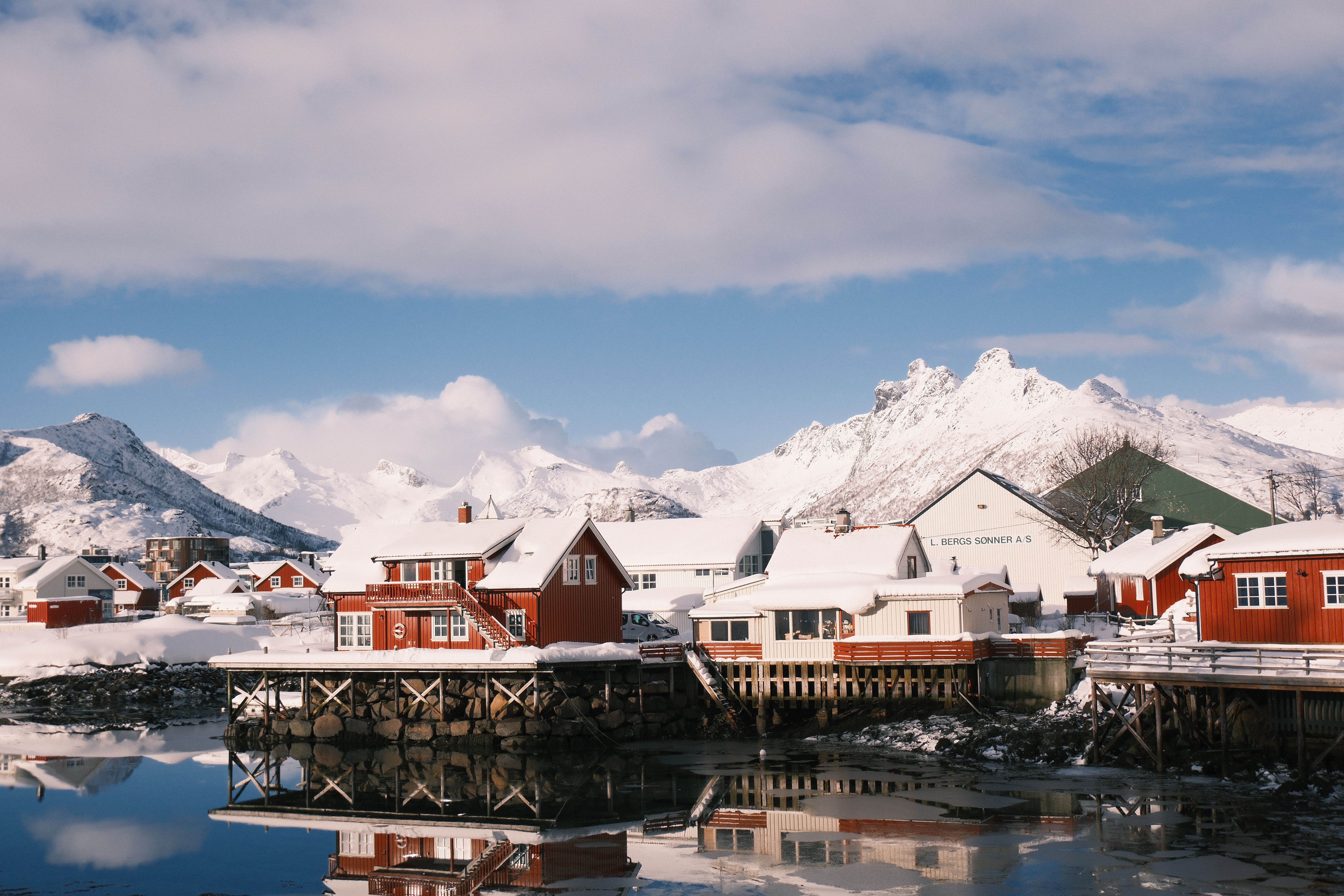 Captivating winter view of the snow-covered coastal town of Svolvær in Norway, featuring traditional red houses and a mountain backdrop.