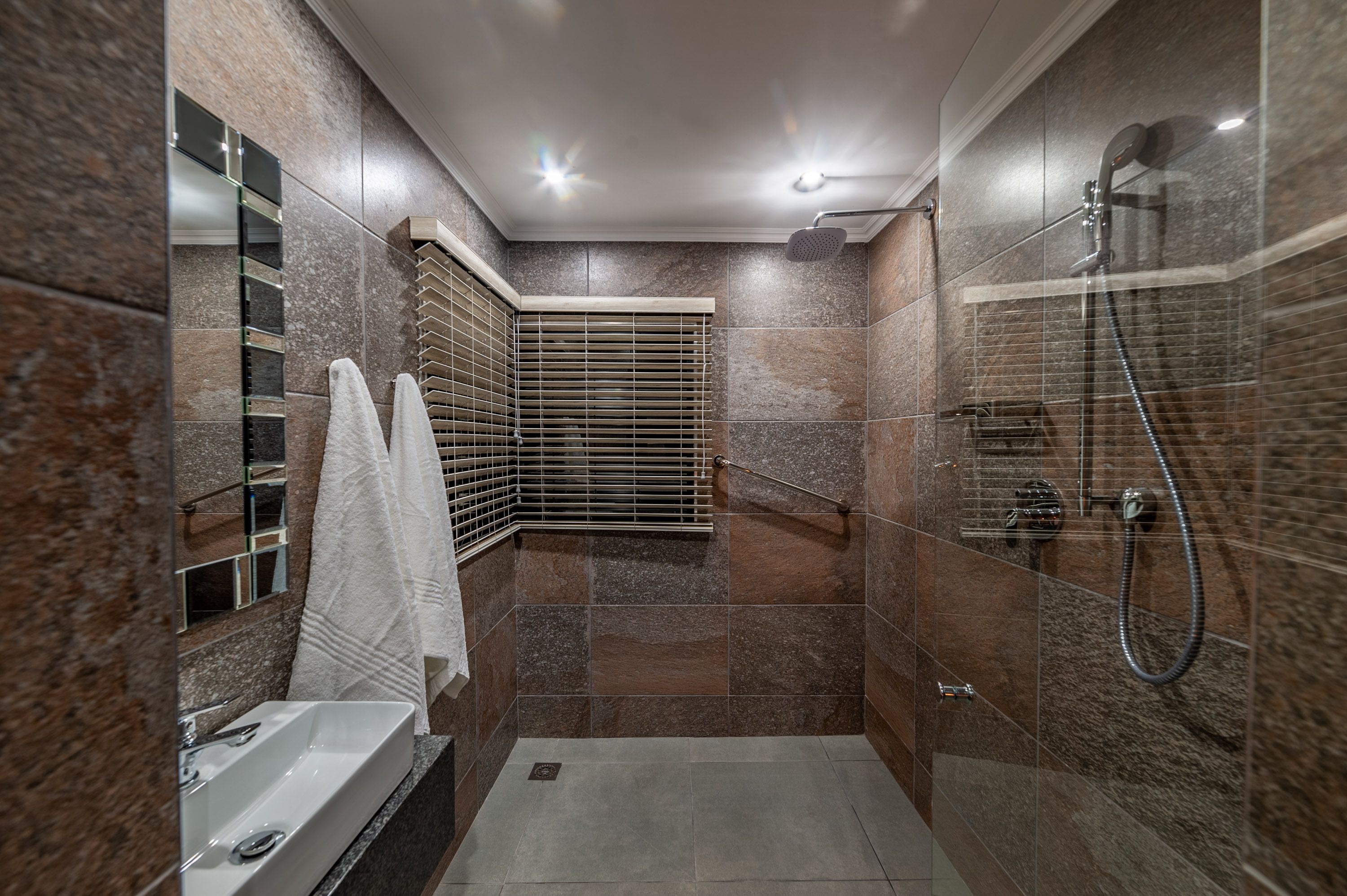 A large walk in shower with white fluffy towels hanging from hooks on the wall