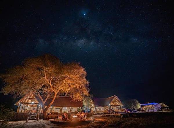 Ndovu Tented Camp illuminated at night with big tree and star filled sky
