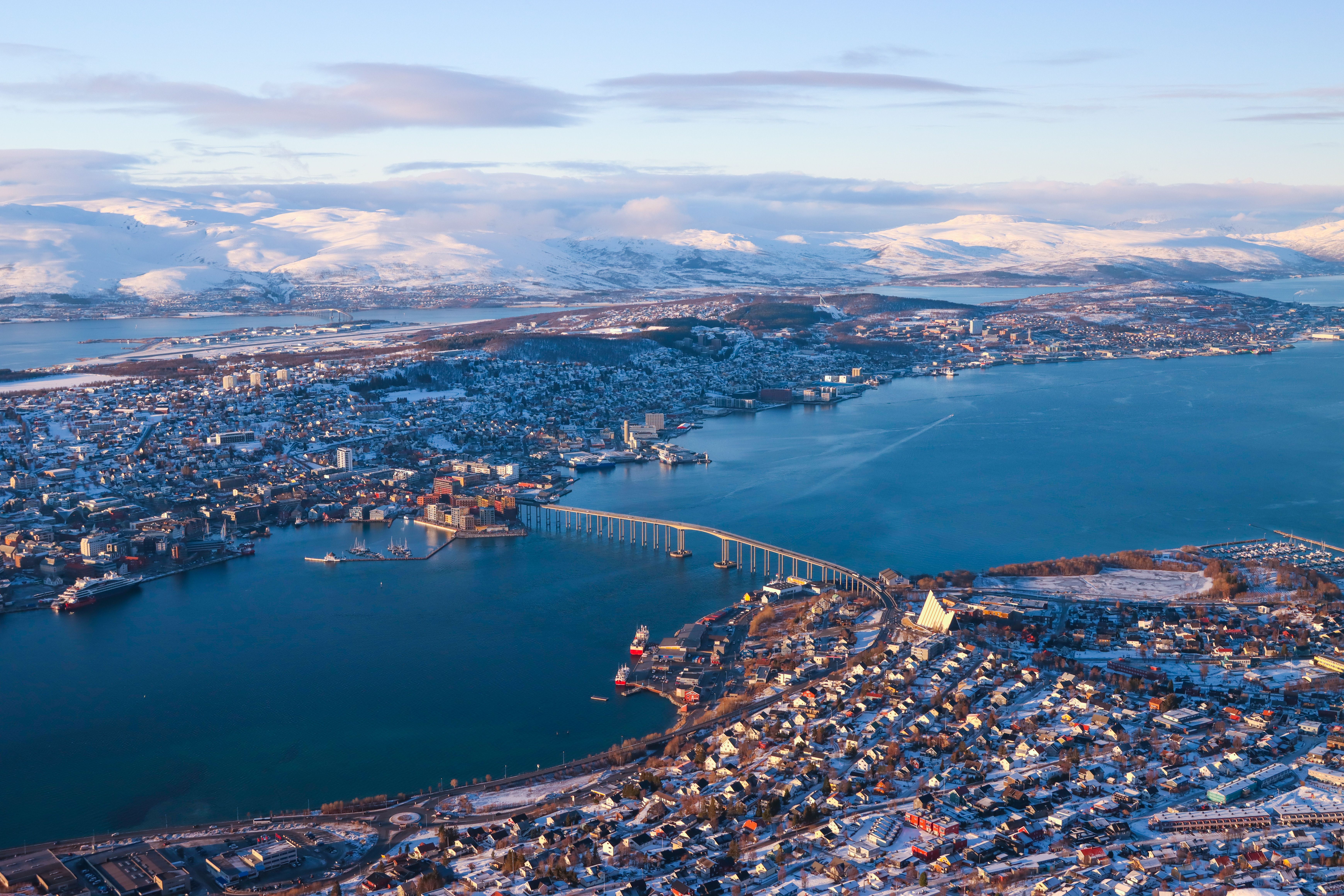 Panoramic aerial view of Tromsø, Norway, showcasing snow-capped mountains and the iconic Arctic Cathedral.