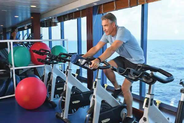 The fitness center aboard the Oceania Insignia with a man on a exercise bicycle with a calm sea of water in the background
