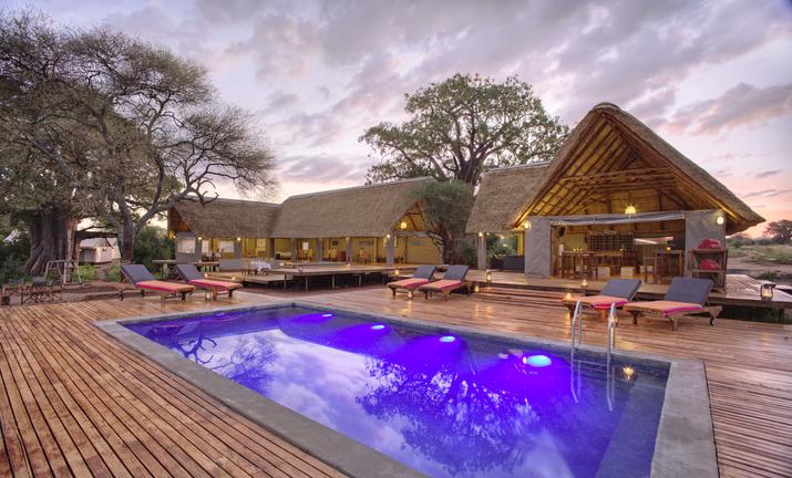 Purple illuminated pool in wooden deck with lodge building in the background