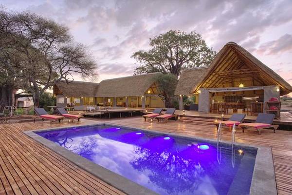 Purple illuminated pool in wooden deck with lodge building in the background