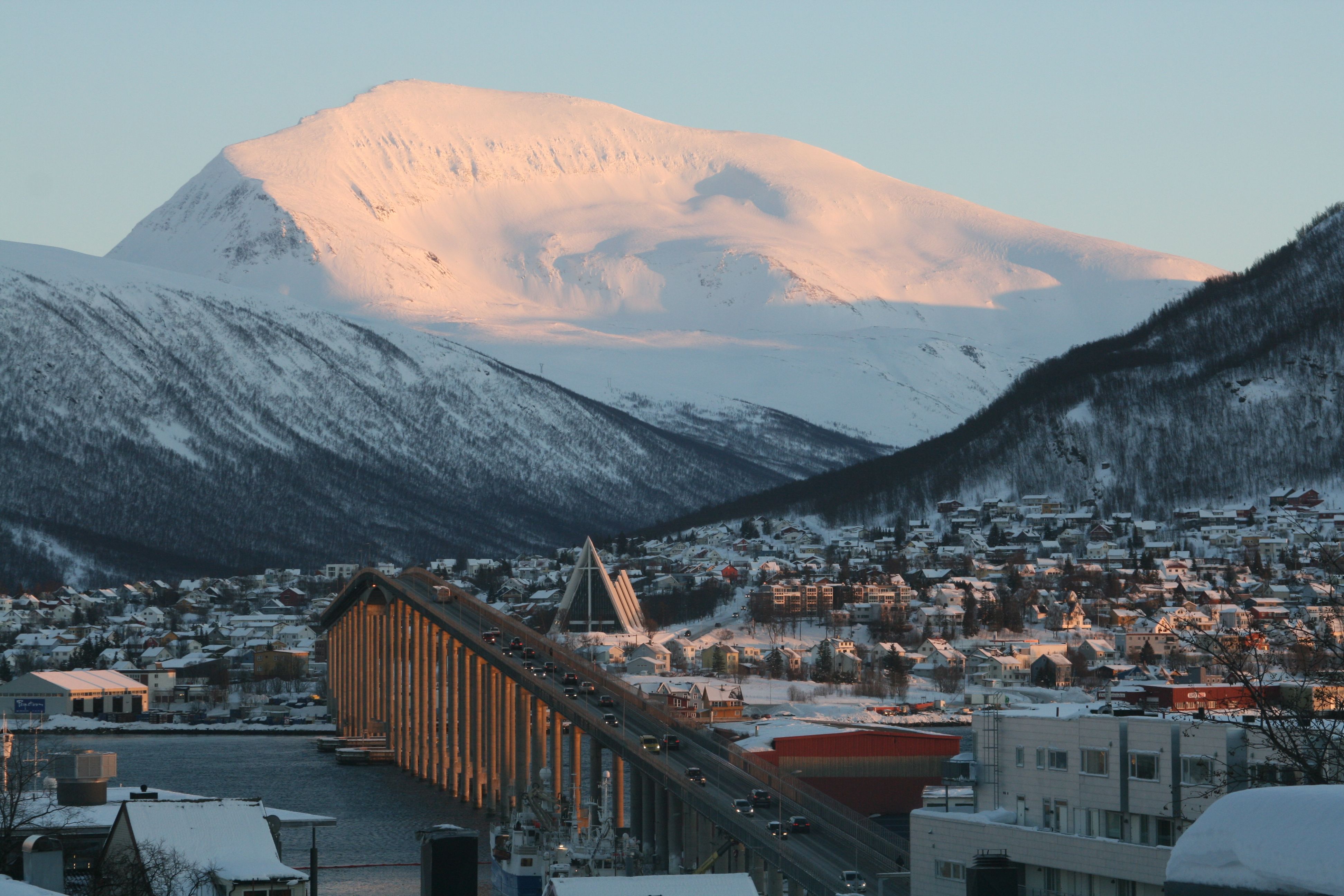 Captivating view of Tromsø, Norway with snow-covered mountains during winter sunset.