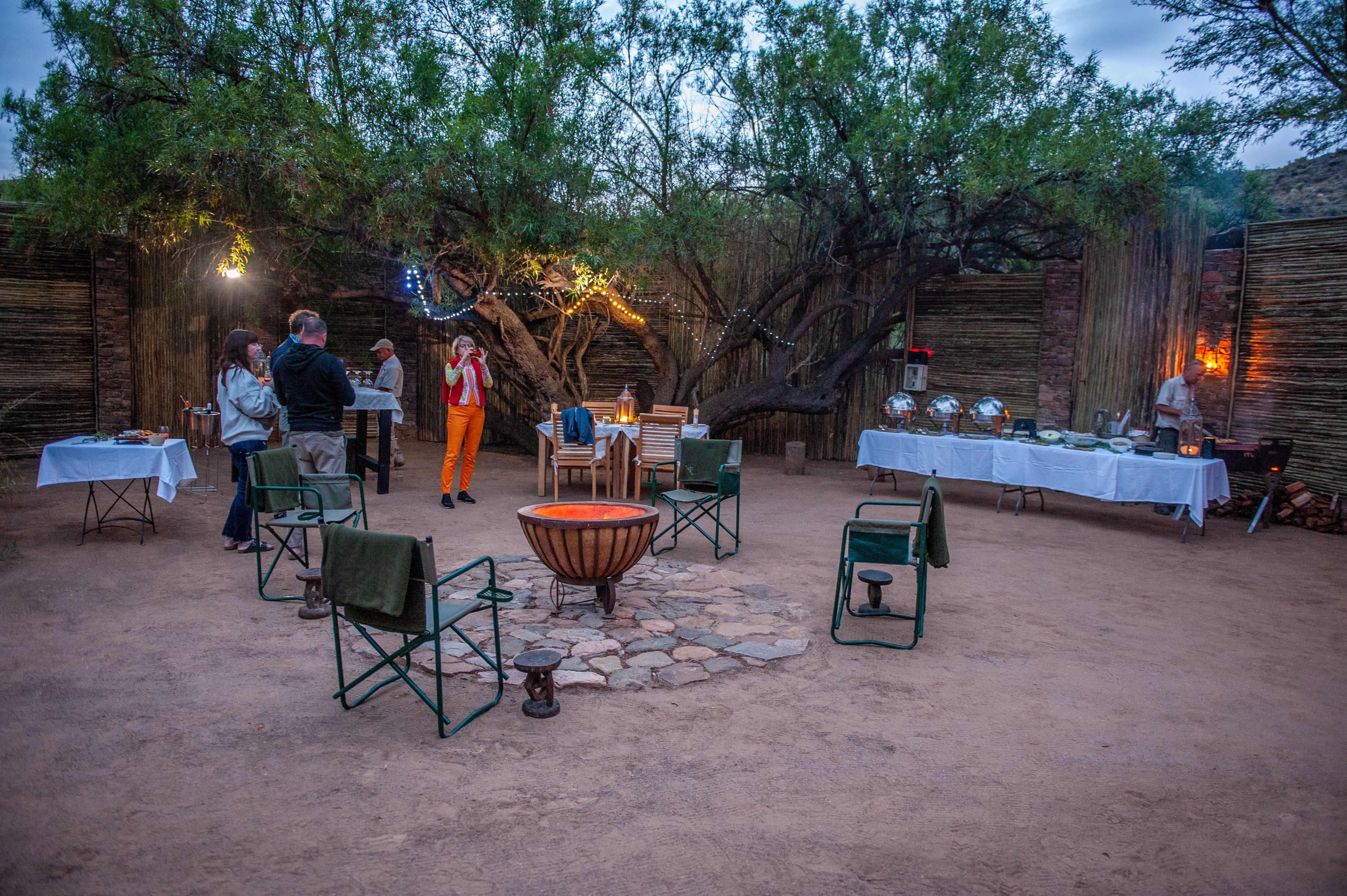 A Boma with a firepit and a buffet with people standing around enjoying drinks