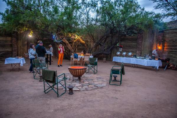 A Boma with a firepit and a buffet with people standing around enjoying drinks