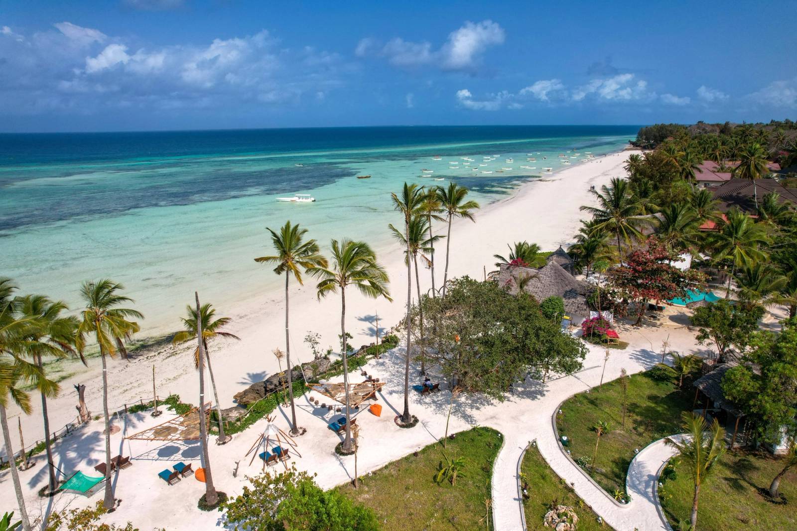 A beach resort in Zanzibar with plam trees and loungers next to a white sandy beach and a turquoise sea