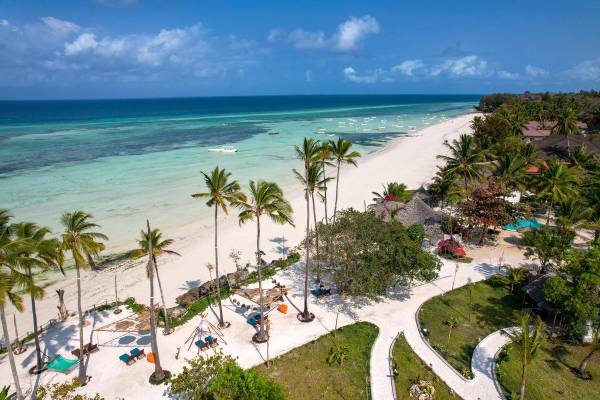 A beach resort in Zanzibar with plam trees and loungers next to a white sandy beach and a turquoise sea