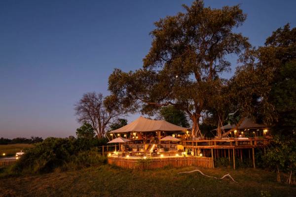 Tuludi tented camp beneath trees at night with lights illuminating the structure