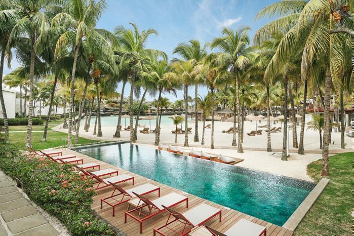 Loungers next to blue pool and white sandy palm tree lined beach