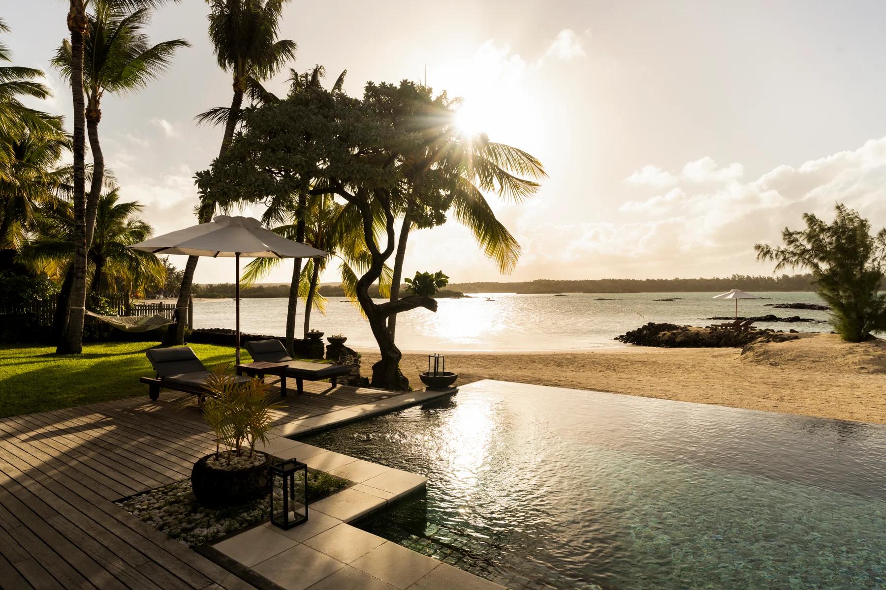 Palm trees and loungers beside an infinity pool overlooking the beach and setting sun