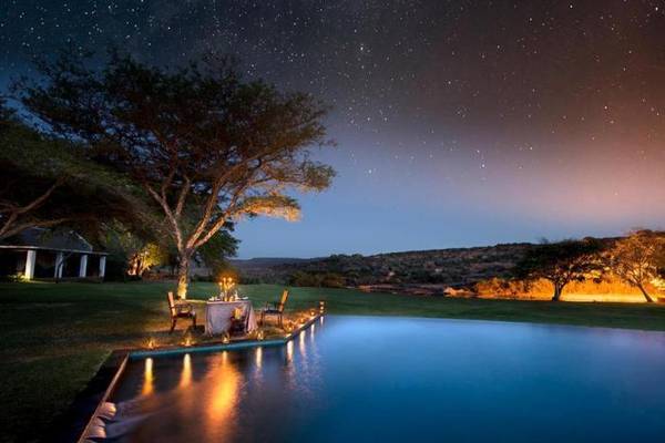 Dining table and chairs next to Bushmans Kloof pool at night