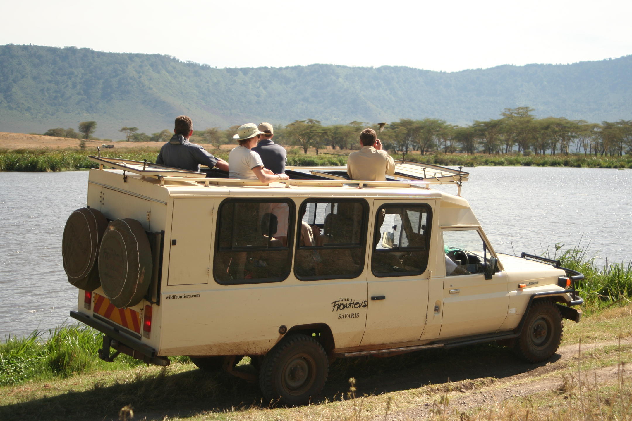 Game drive vehicle with people looking out the top over lake and mountains